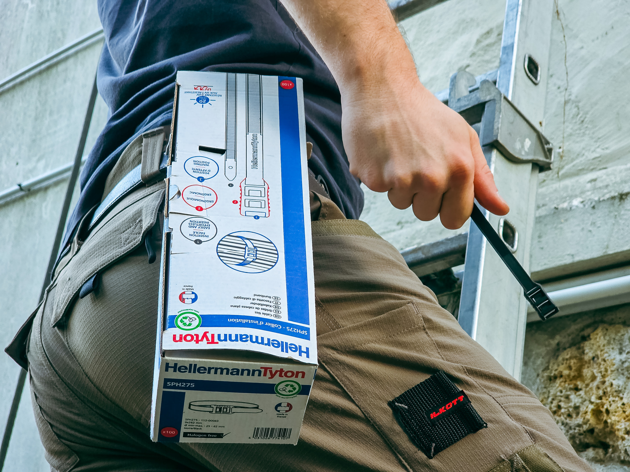 Box mit HellermannTyton-Kabelbindern SPH275 in der Gesäßtasche einer beigen Ilkott-Arbeitshose, Ilkott-Aufnäher sichtbar