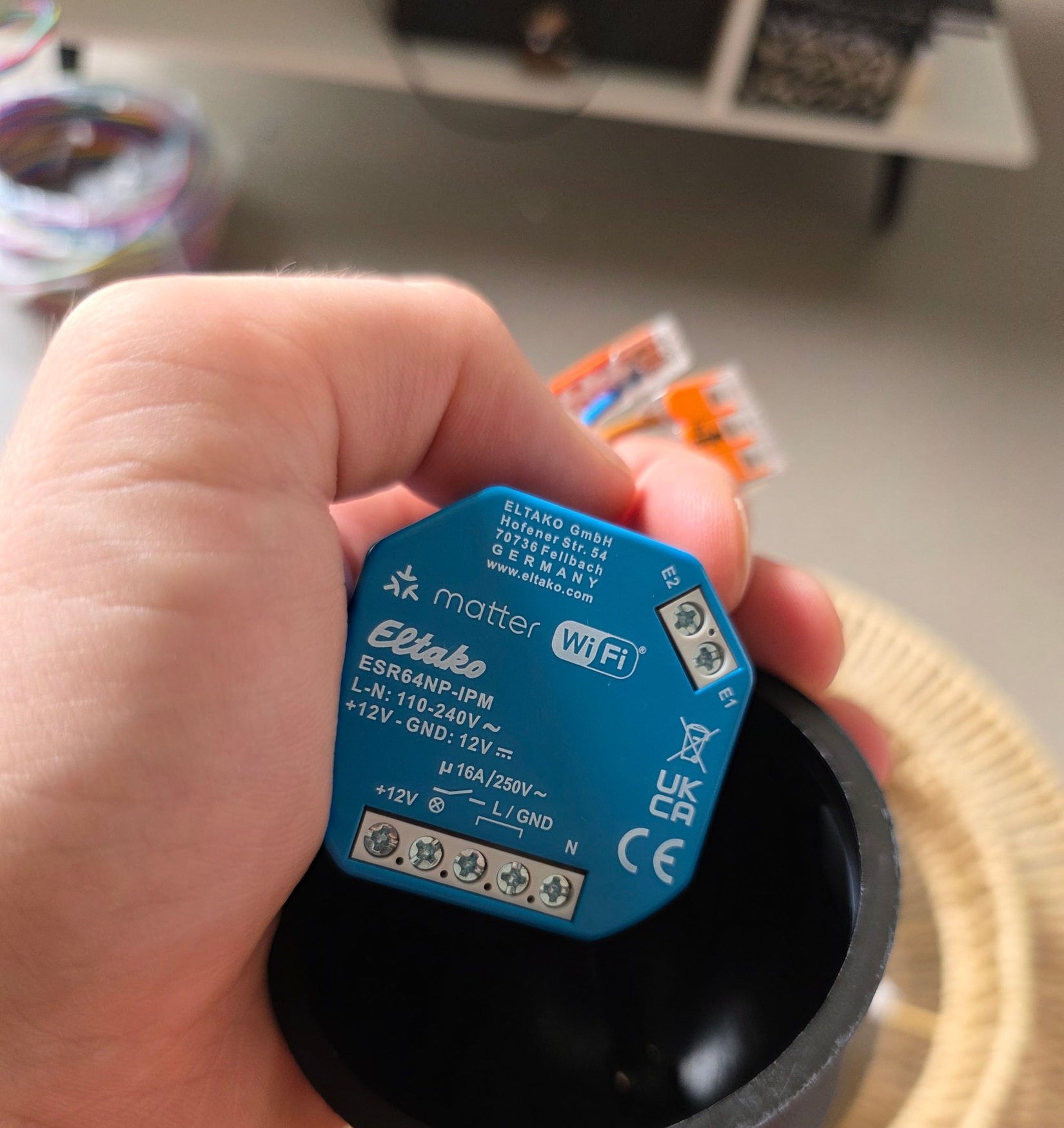 Micromodule Eltako ESR64NP-IPM tenu en main, avec ses repères E1 et E2 et sa rangée de bornes à vis.