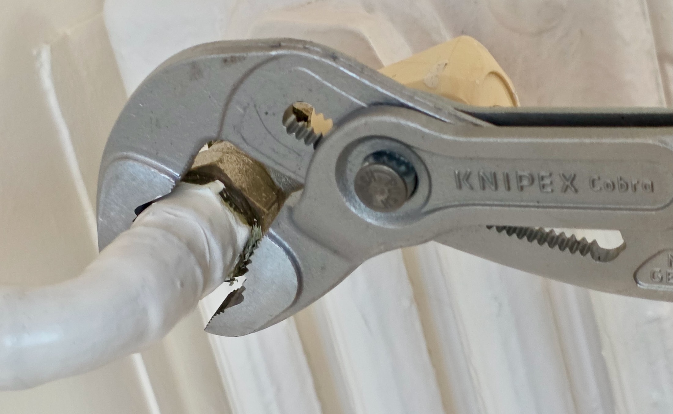 Gros plan sur la mâchoire de la pince Knipex Cobra 87 03 300, en prise sur un écrou de radiateur