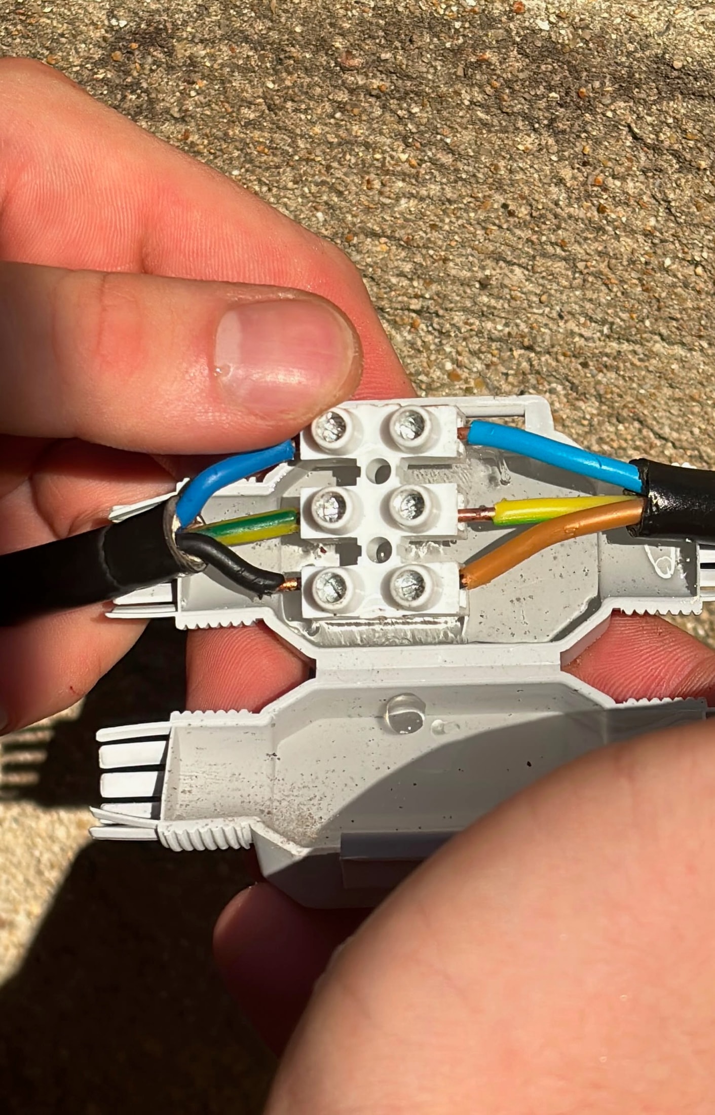 Connecteur étanche gris ouvert tenu en main avec son bornier blanc à vis et des fils colorés raccordés