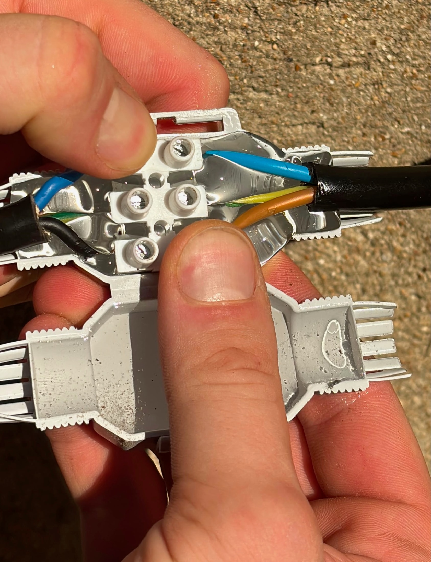 Connecteur étanche gris ouvert tenu en main avec un domino dans le gel et des fils colorés raccordés