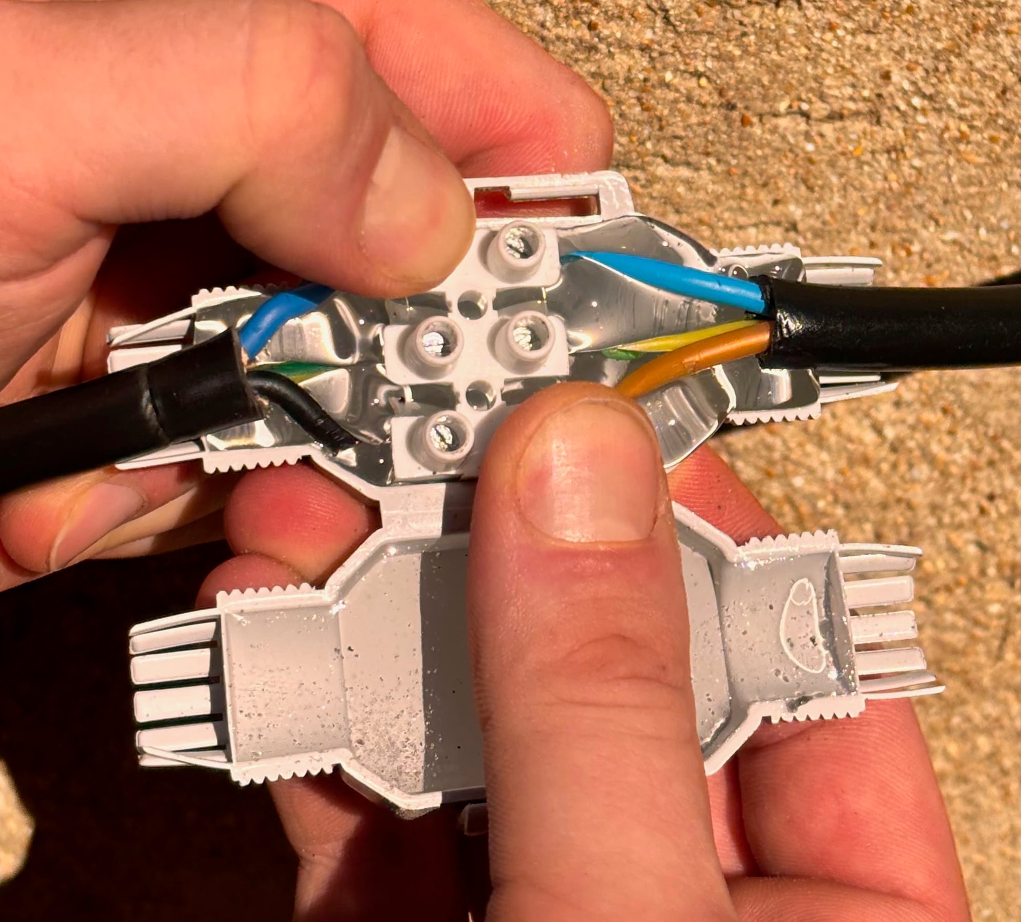 Connecteur étanche ouvert avec deux câbles noirs raccordés dans un bornier à vis