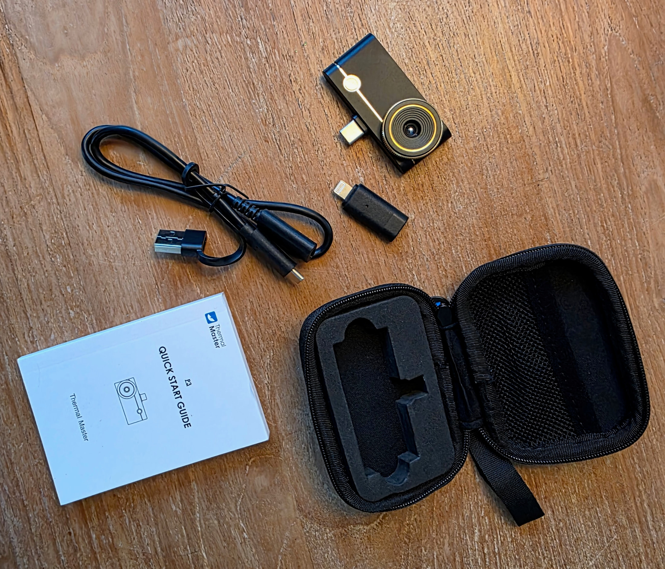 Module Thermal Master P3, câble USB, adaptateur Lightning, étui et guide de démarrage rapide posés sur une table en bois