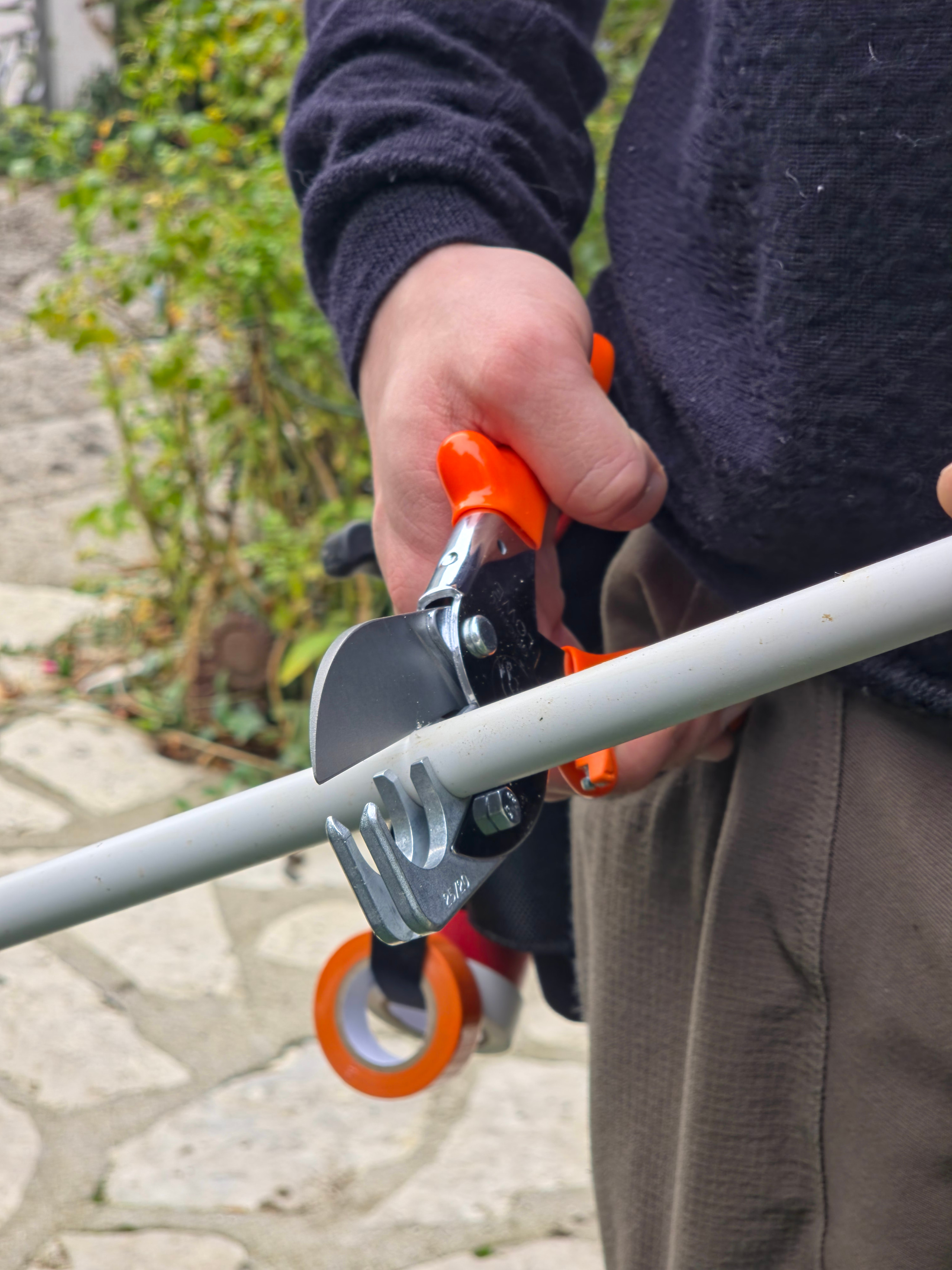 Tube plastique blanc tenu en main dans un jardin, avant la coupe