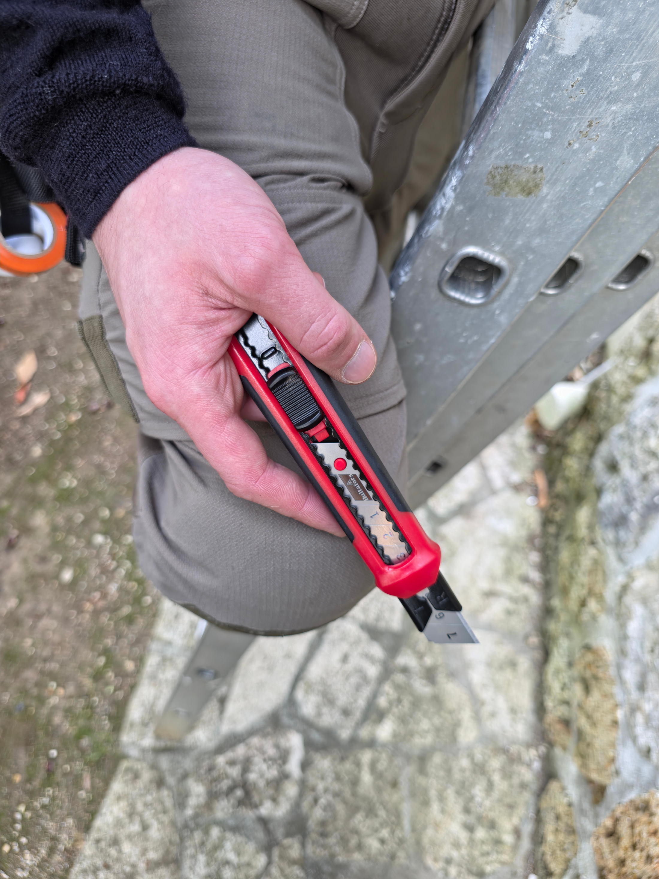 Cutter Hultafors en main, corps rouge et noir, lame à segments déployée