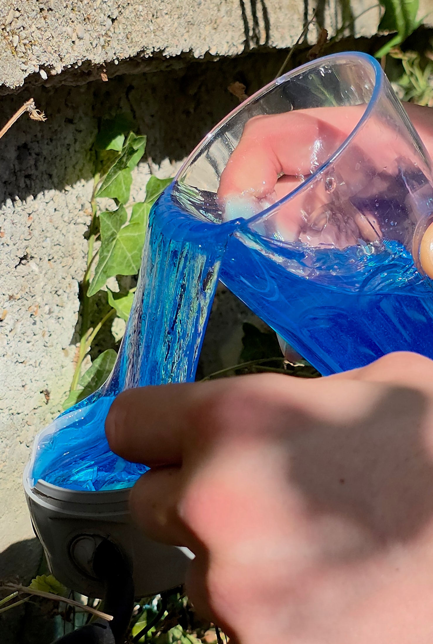 Doigt touchant le Magic Gel bleu dans une boîte de dérivation ronde qui se remplit de gel versé depuis un verre tenu à la main