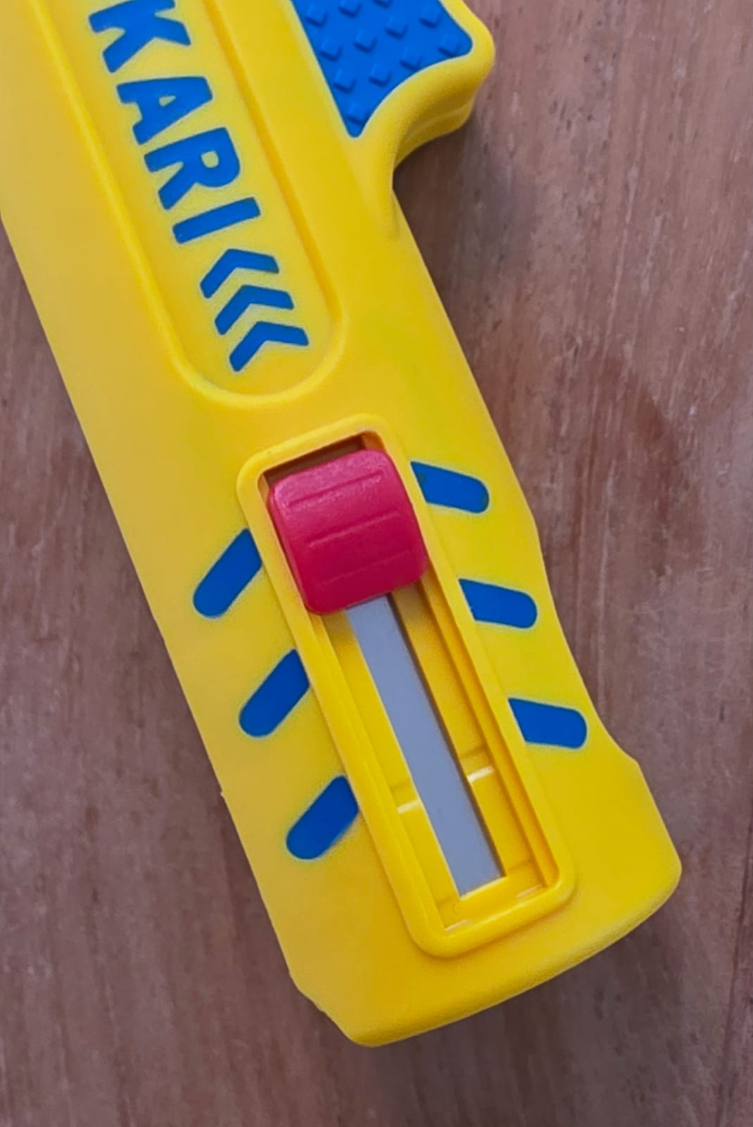 Gros plan sur le bouton rouge et la lame du dénudeur Jokari jaune posé sur du bois