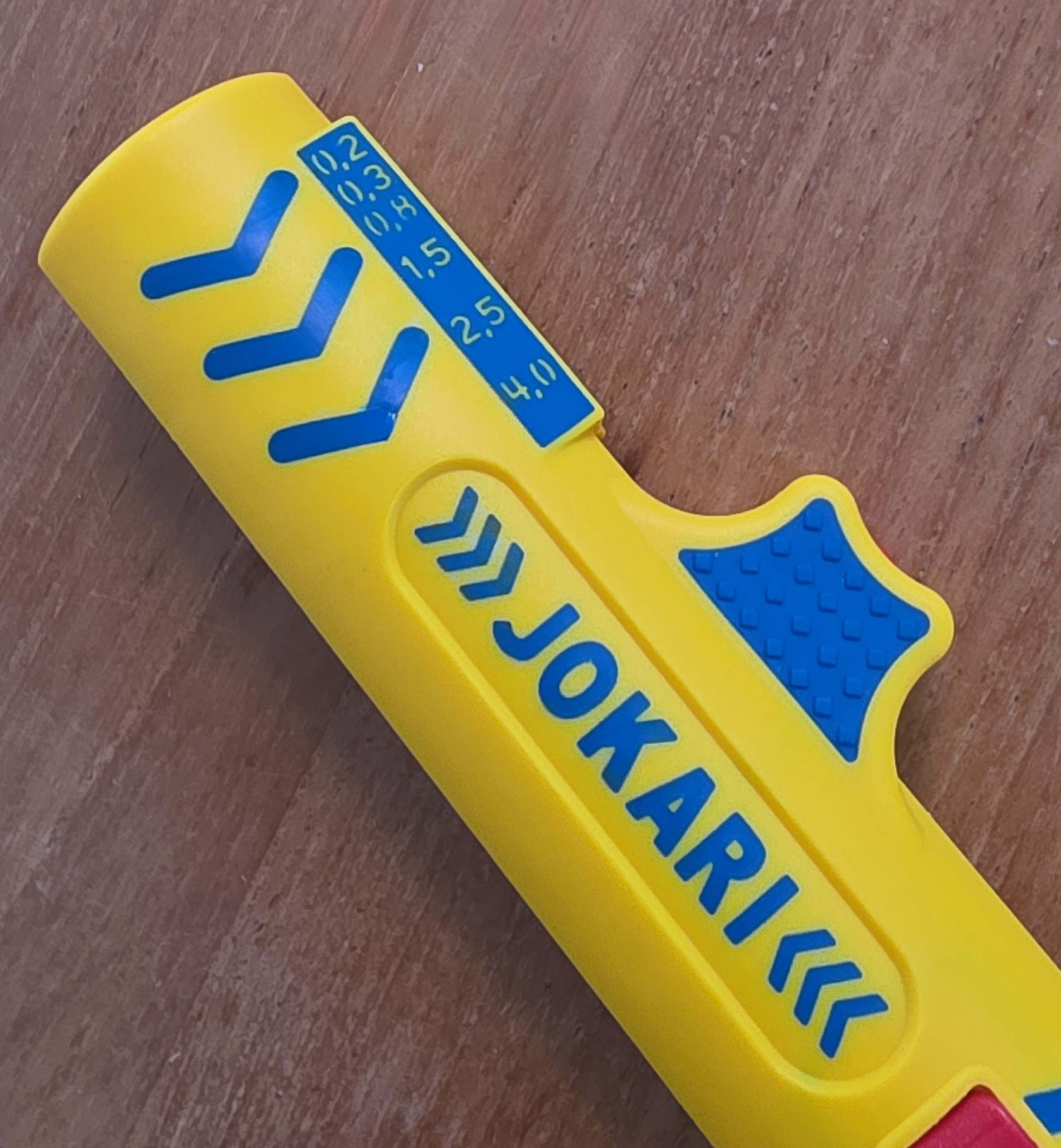 Vue du dessus de la pince à dénuder Jokari jaune et bleue sur une table en bois, graduations bleues visibles