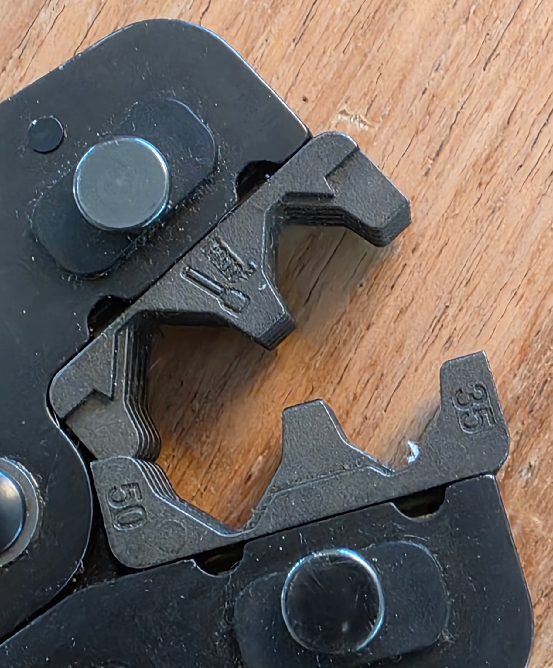 Gros plan sur les mâchoires de sertissage noires d’une pince Klauke avec les gravures 35 et 50 embossées