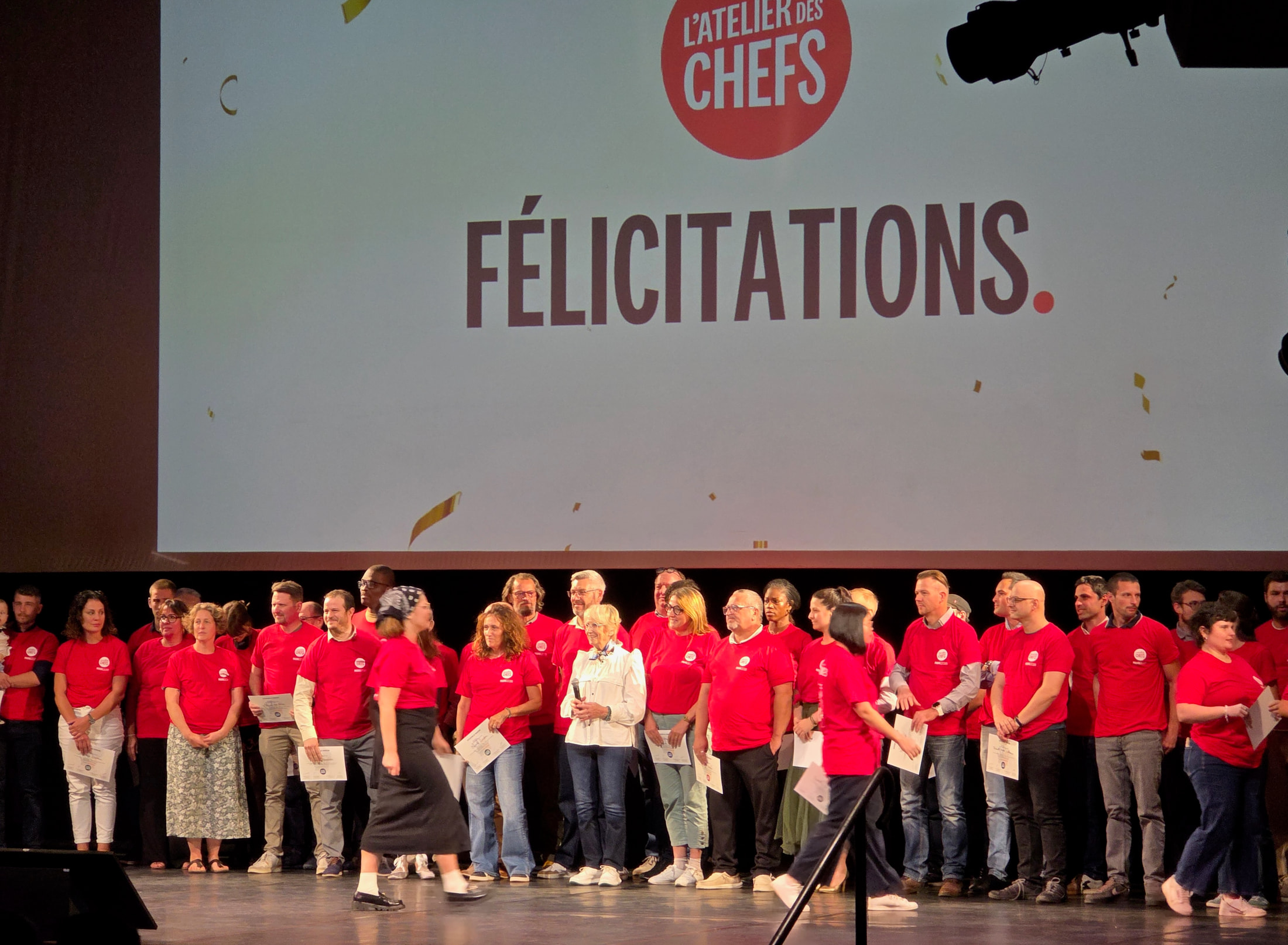 Groupe de diplômés en t-shirts rouges L’Atelier des Chefs sur la scène du Théâtre Mogador