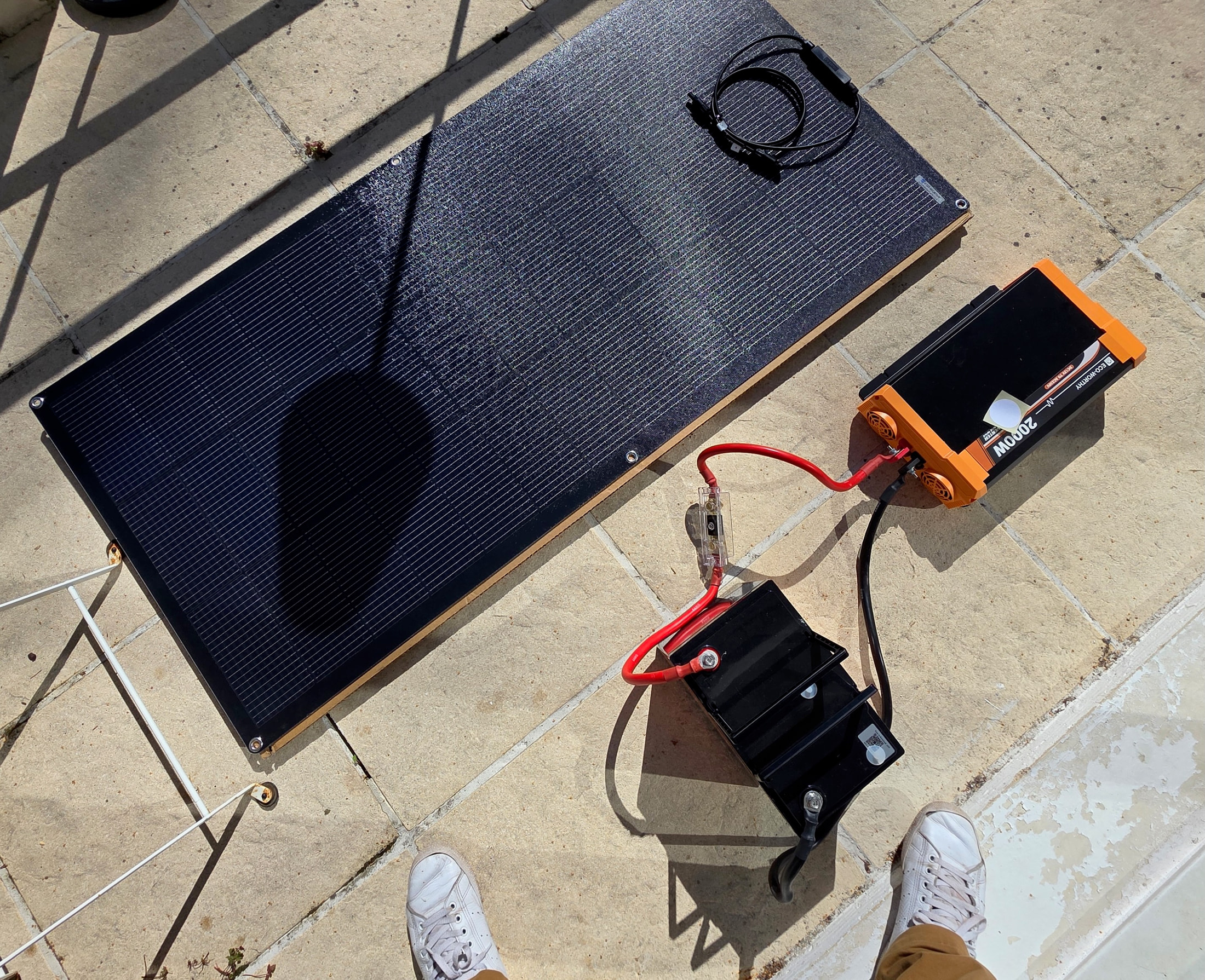 Kit solaire ECO-WORTHY complet posé sur une terrasse carrelée, vu du dessus : panneau, batterie et onduleur