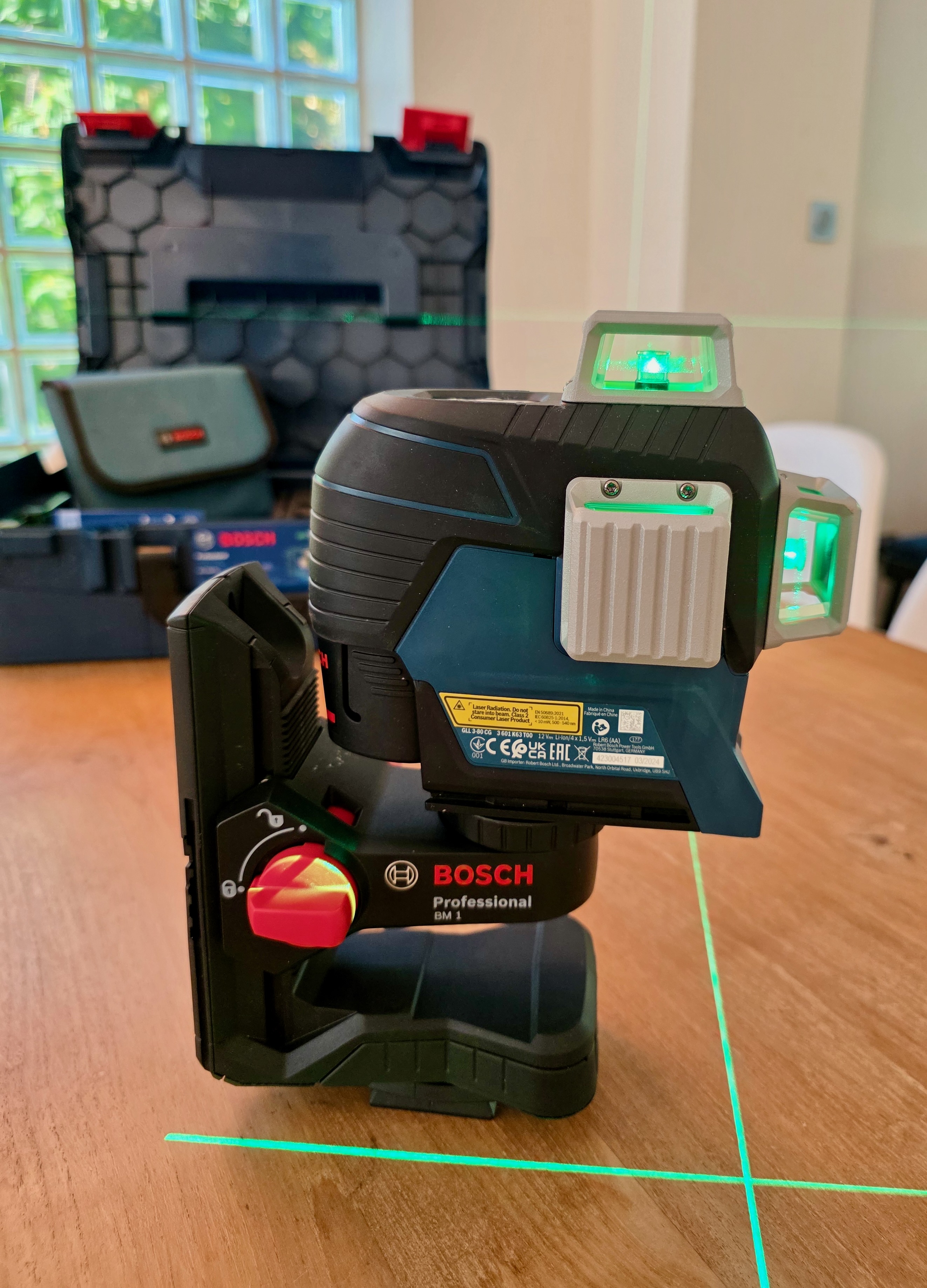 Niveau laser Bosch posé sur une table, allumé, projetant une ligne laser verte sur le mur