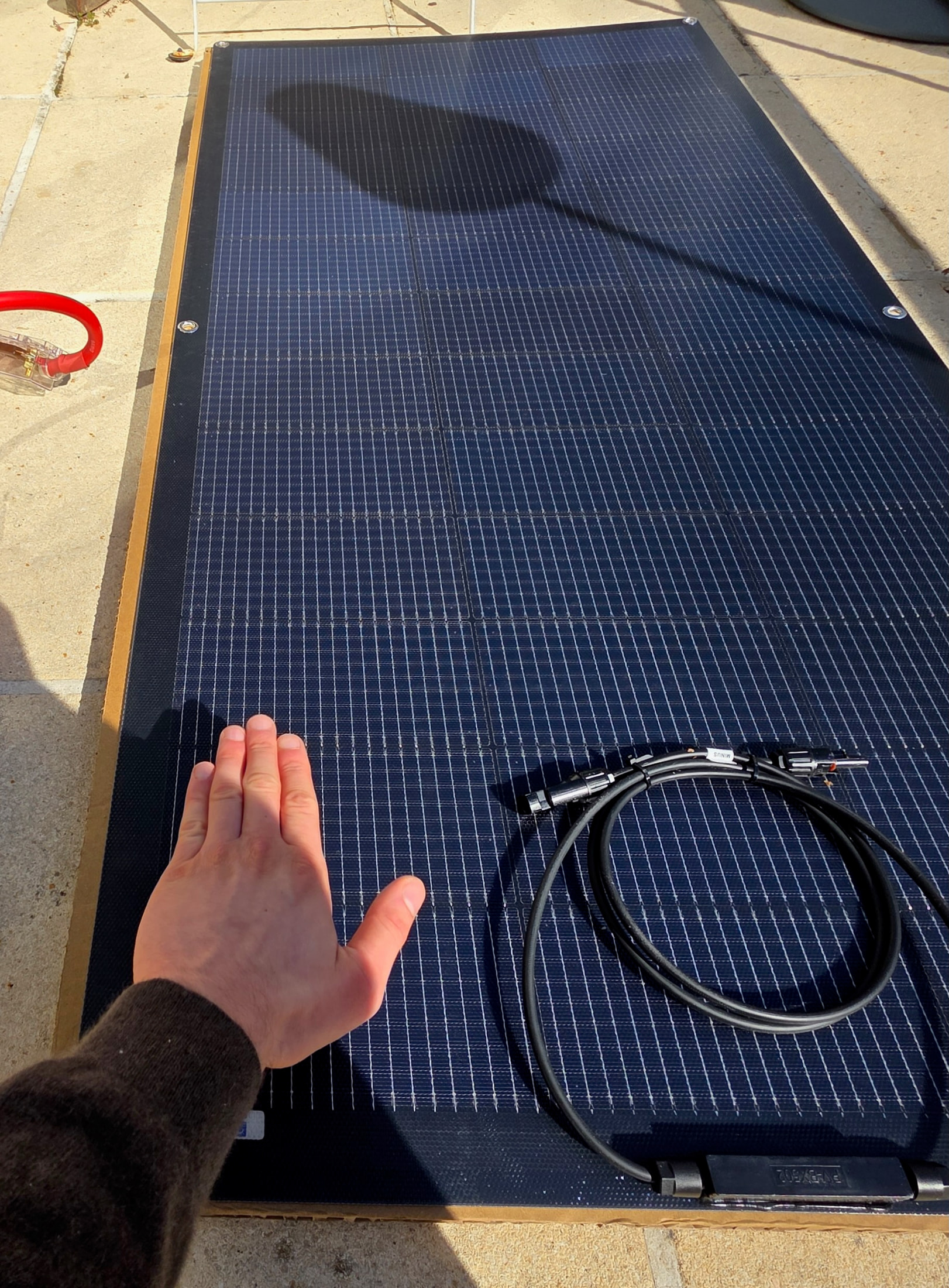 Main présentant le panneau solaire ECO-WORTHY avec l’onduleur et la batterie du kit à côté