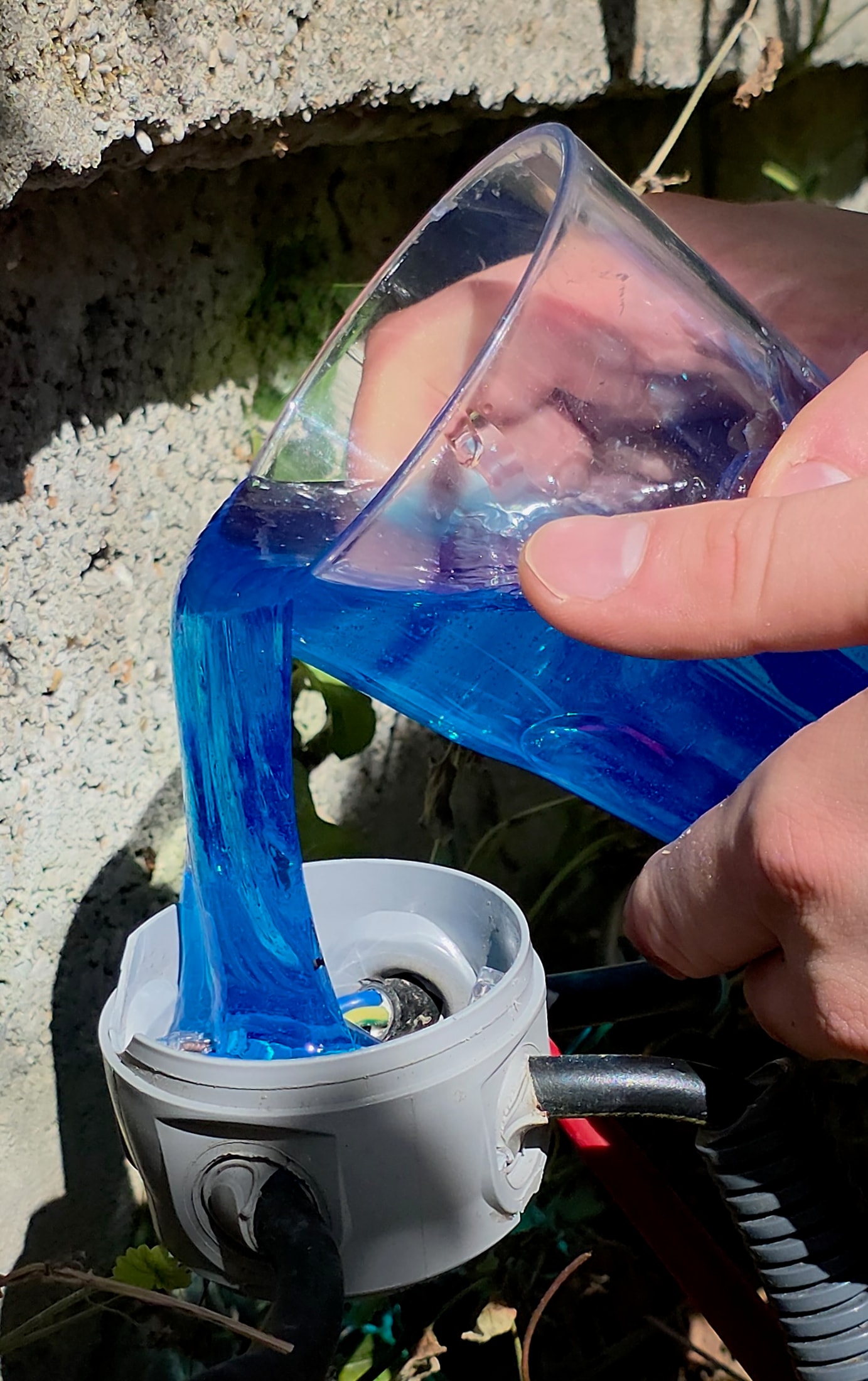 Mains versant le gel bleu Magic Gel dans une boîte de dérivation ronde grise en extérieur sur un mur en béton
