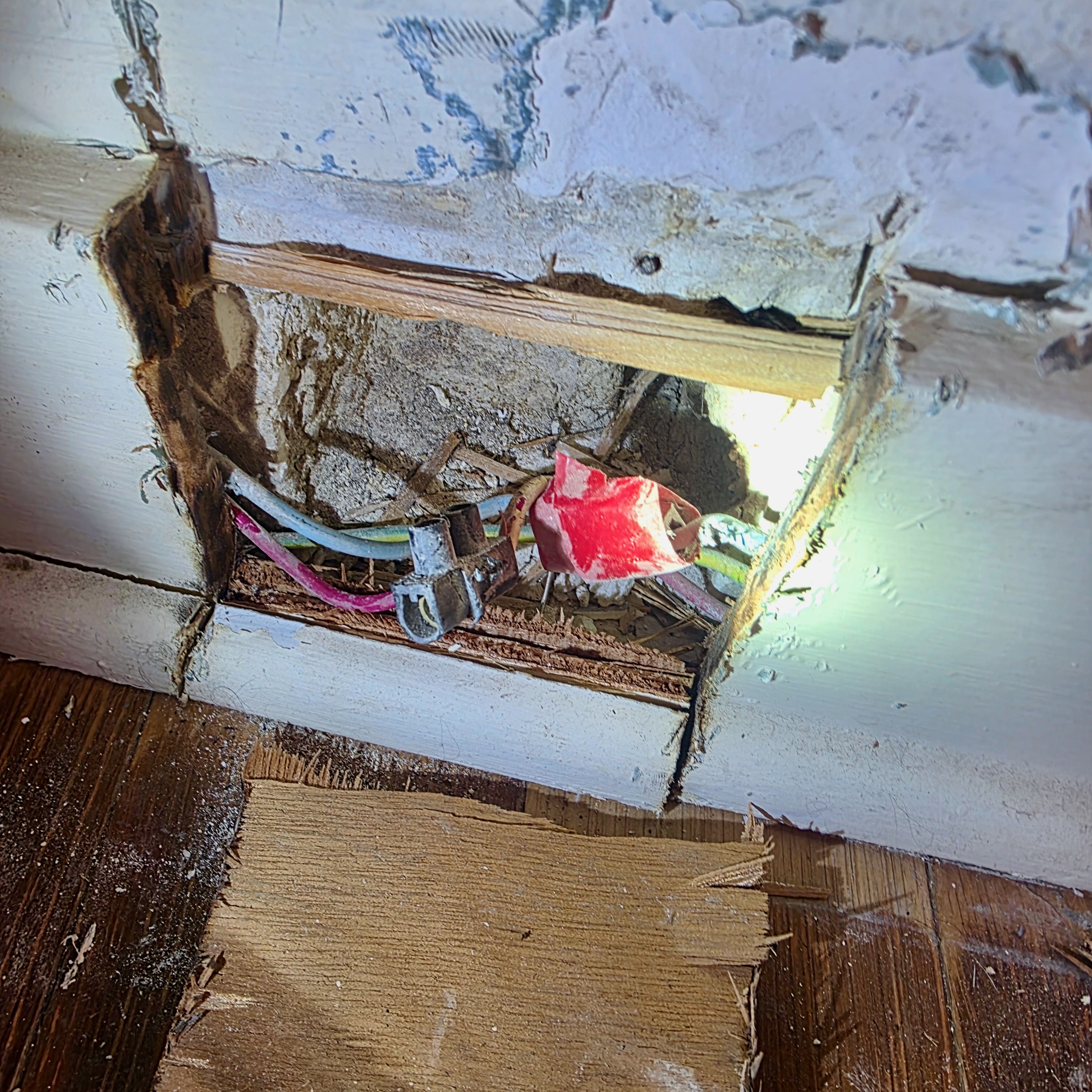 Câblage électrique vétuste dissimulé derrière une plinthe, avec un domino et une connexion enveloppée de ruban isolant