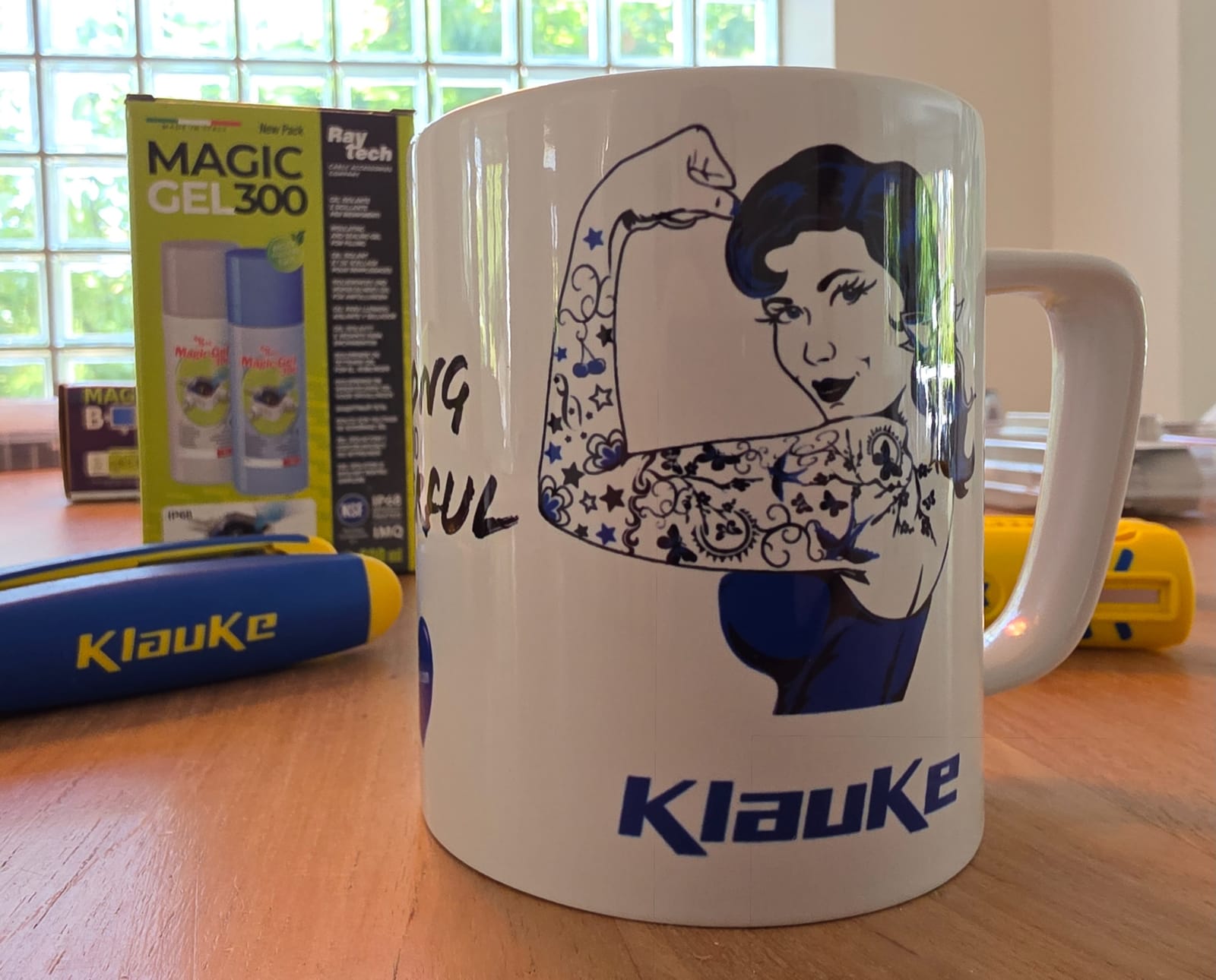 Mug blanc Klauke avec un dessin de femme au bras levé, une boîte de gel Raytech en arrière-plan