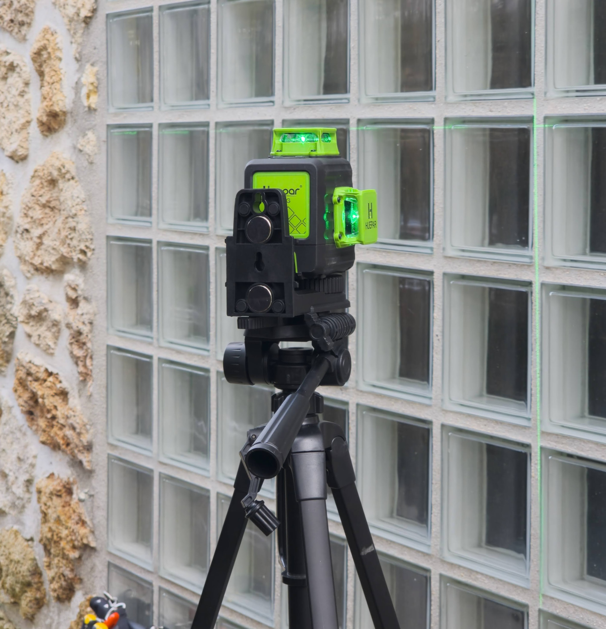 Lignes vertes du laser Huepar sur un mur en briques et verre