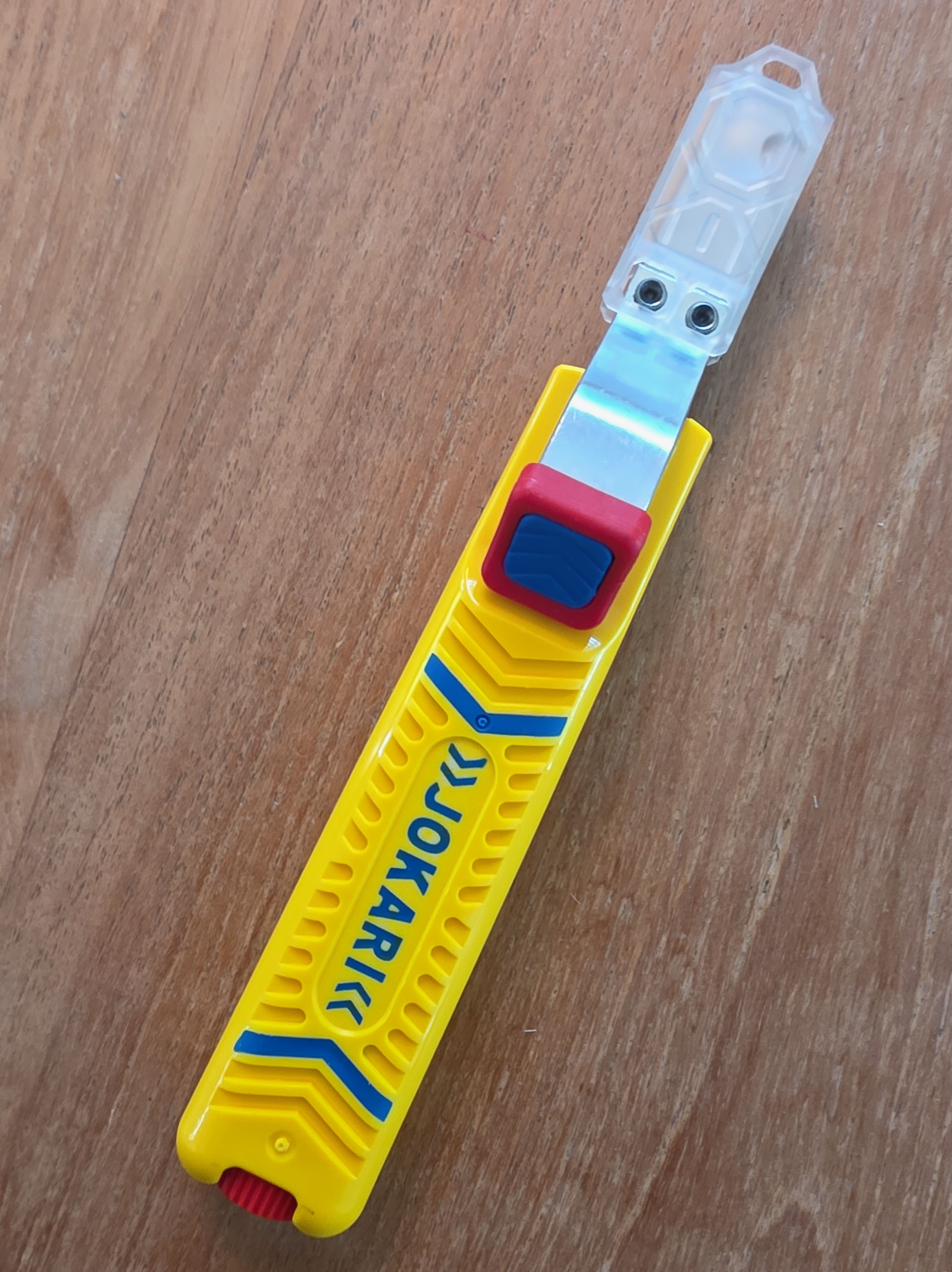 Couteau à dégainer Jokari No. 28H hors emballage posé sur une table en bois, lame crochet déployée avec son capuchon de protection