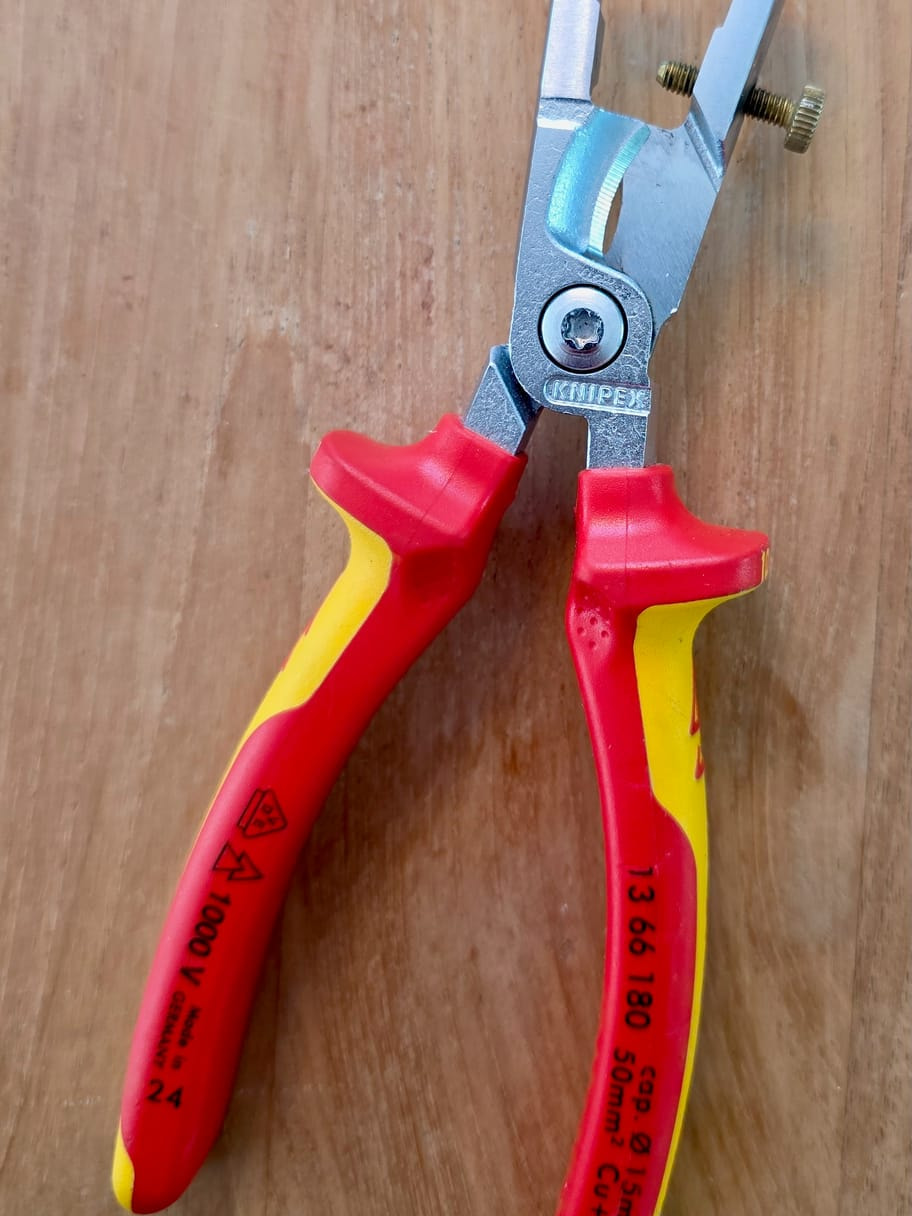 Pince à dénuder Knipex 13 66 180 posée sur une table en bois, manche rouge et jaune avec marquage double triangle, 1000 V et référence visibles
