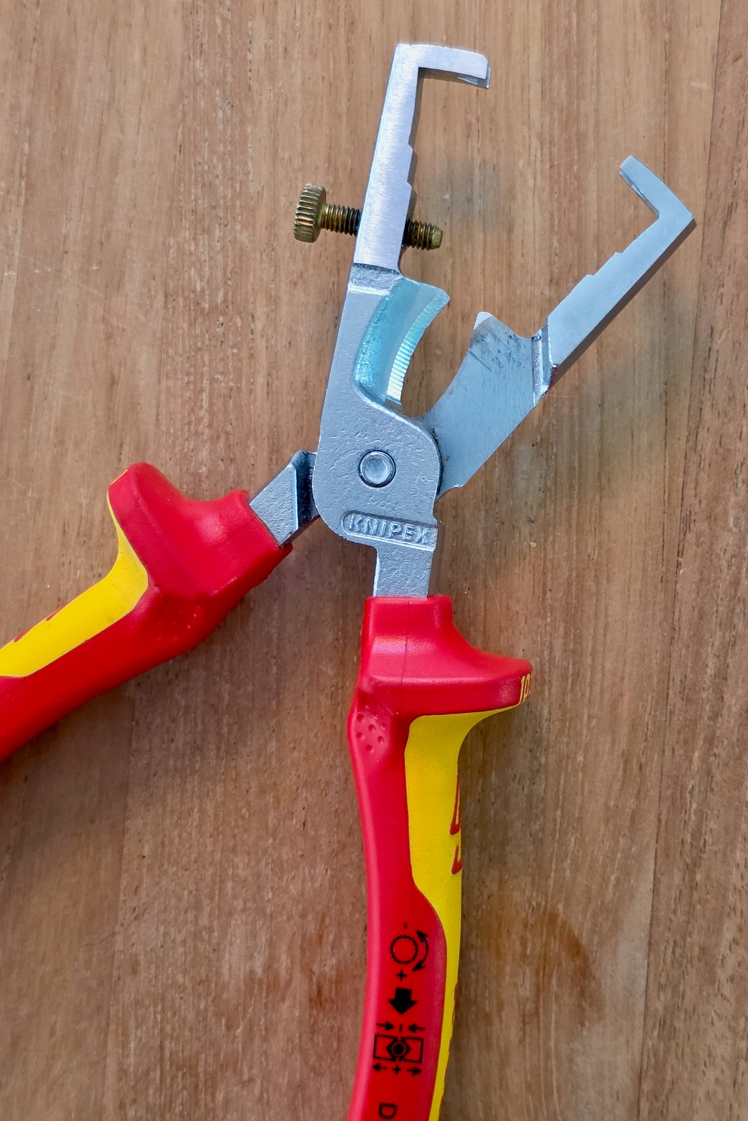 Pince à dénuder Knipex 13 66 180 VDE posée sur table, mâchoire ouverte et écrou de réglage visibles