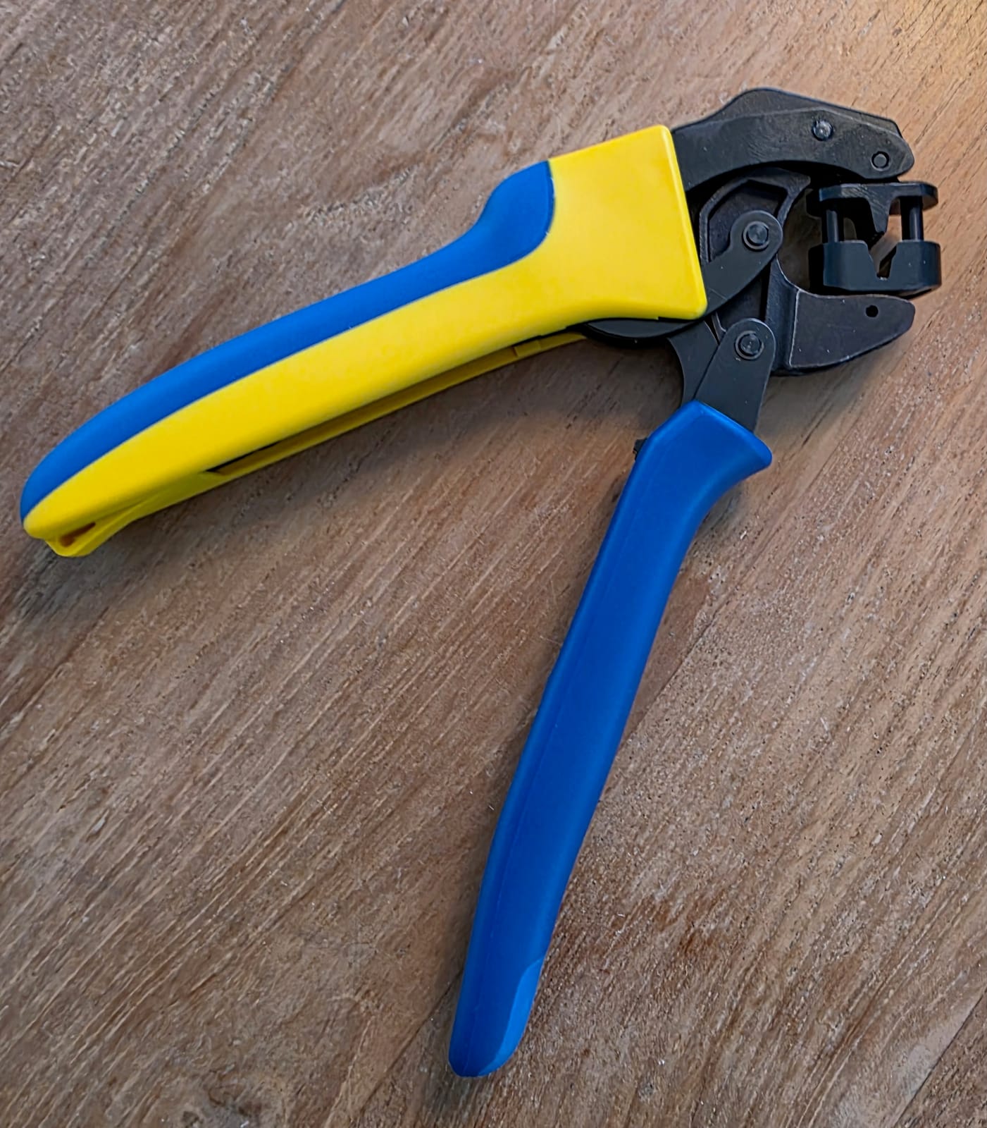 Pince Klauke K32 ouverte sur un plan de travail en bois, poignées bleu et jaune et tête de sertissage noire