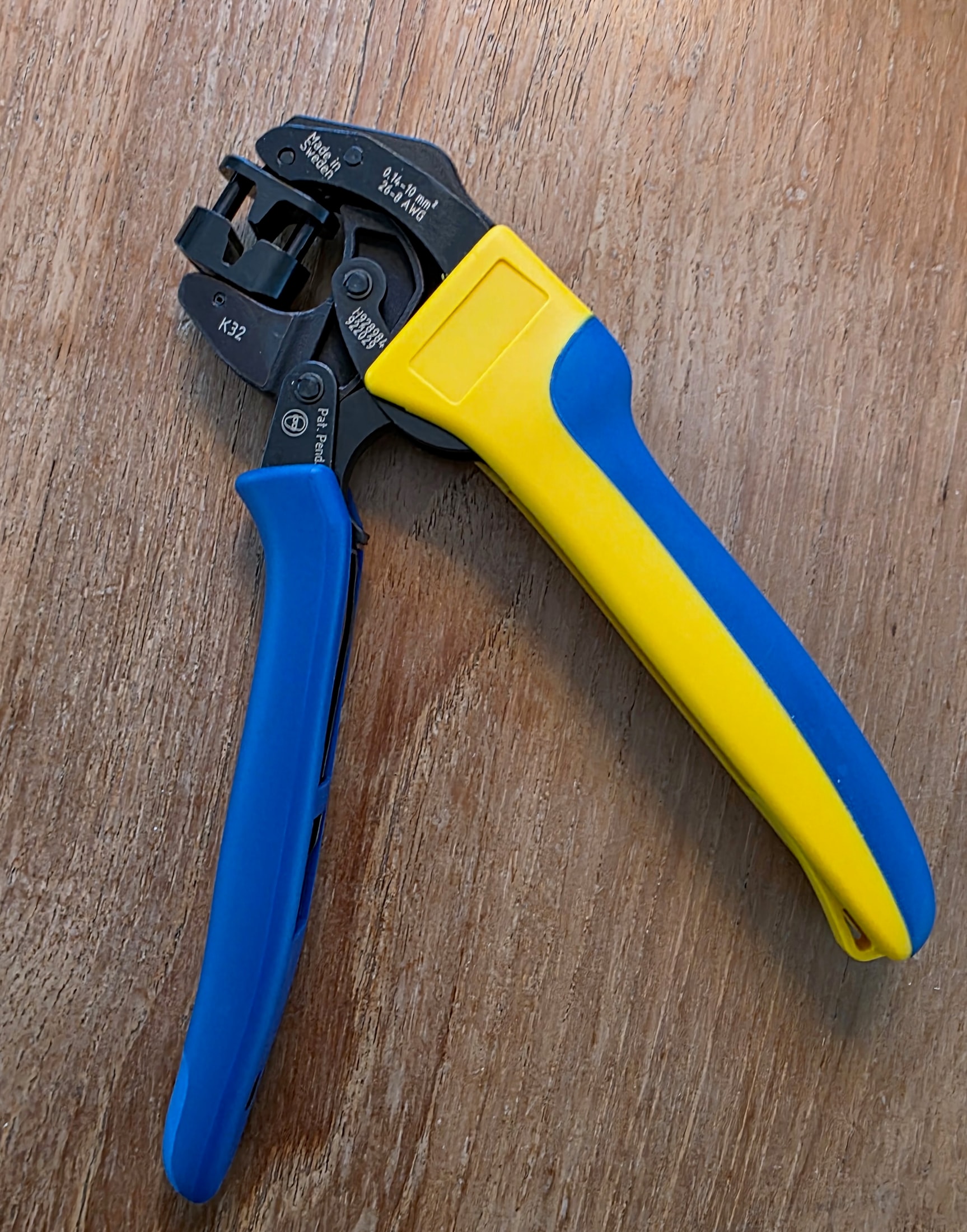 Pince à sertir Klauke K 32 complète posée sur une surface en bois, poignées bleue et jaune, gravure Made in Sweden sur la tête