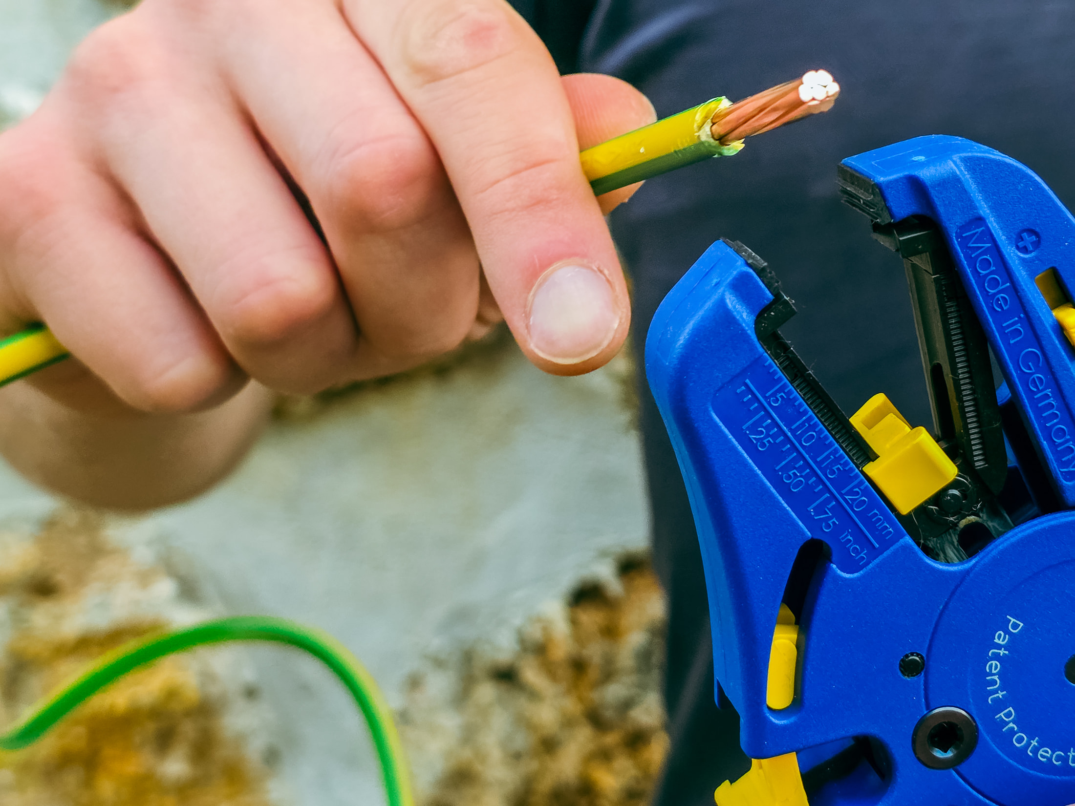 Pince à dénuder automatique Klauke K43/3 bleue et jaune tenue avec un conducteur vert et jaune dénudé