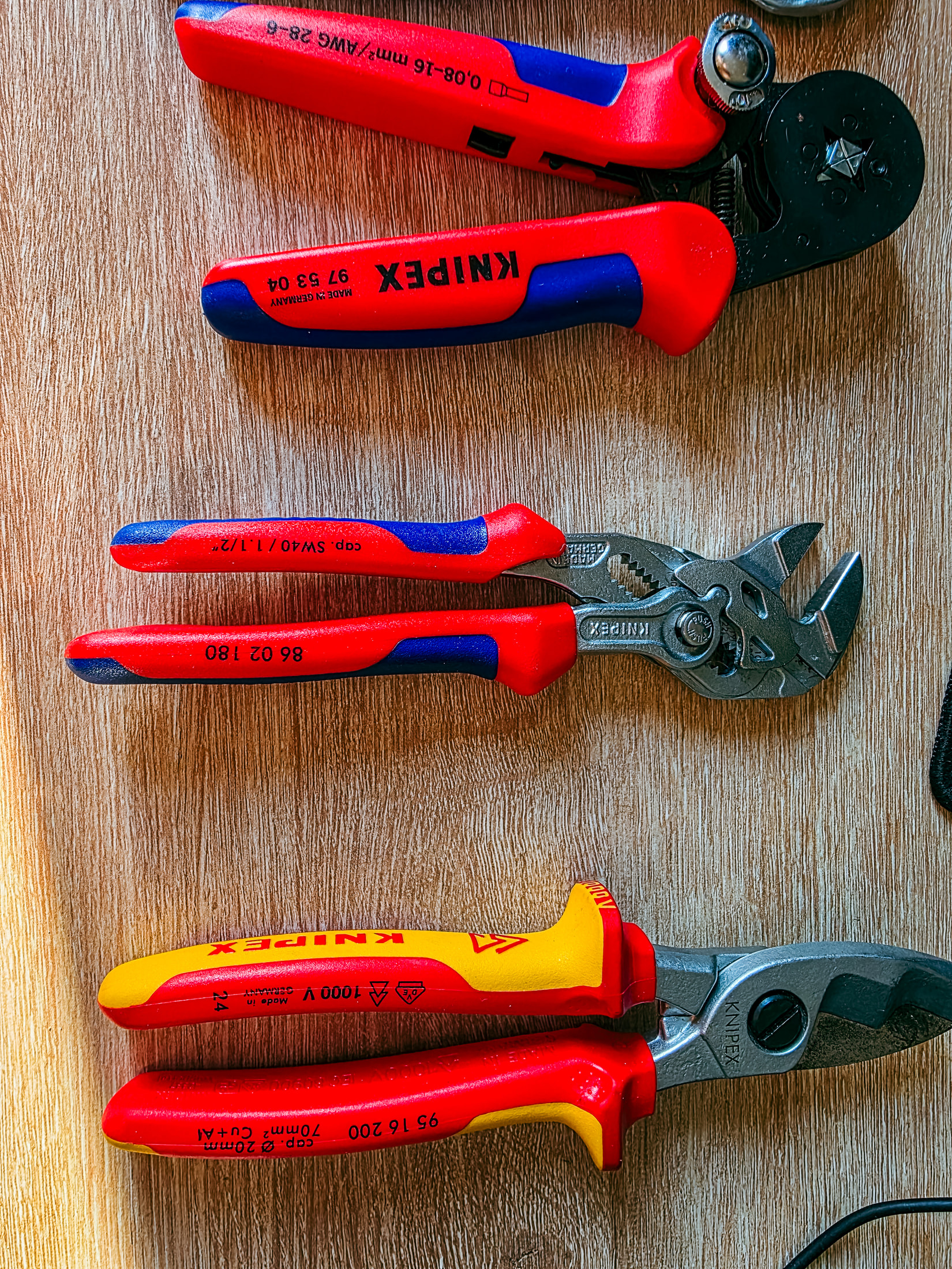 Trois pinces Knipex posées sur du bois : pince à sertir 97 53 04, pince-clé 86 02 180 et coupe-câble 95 16 200