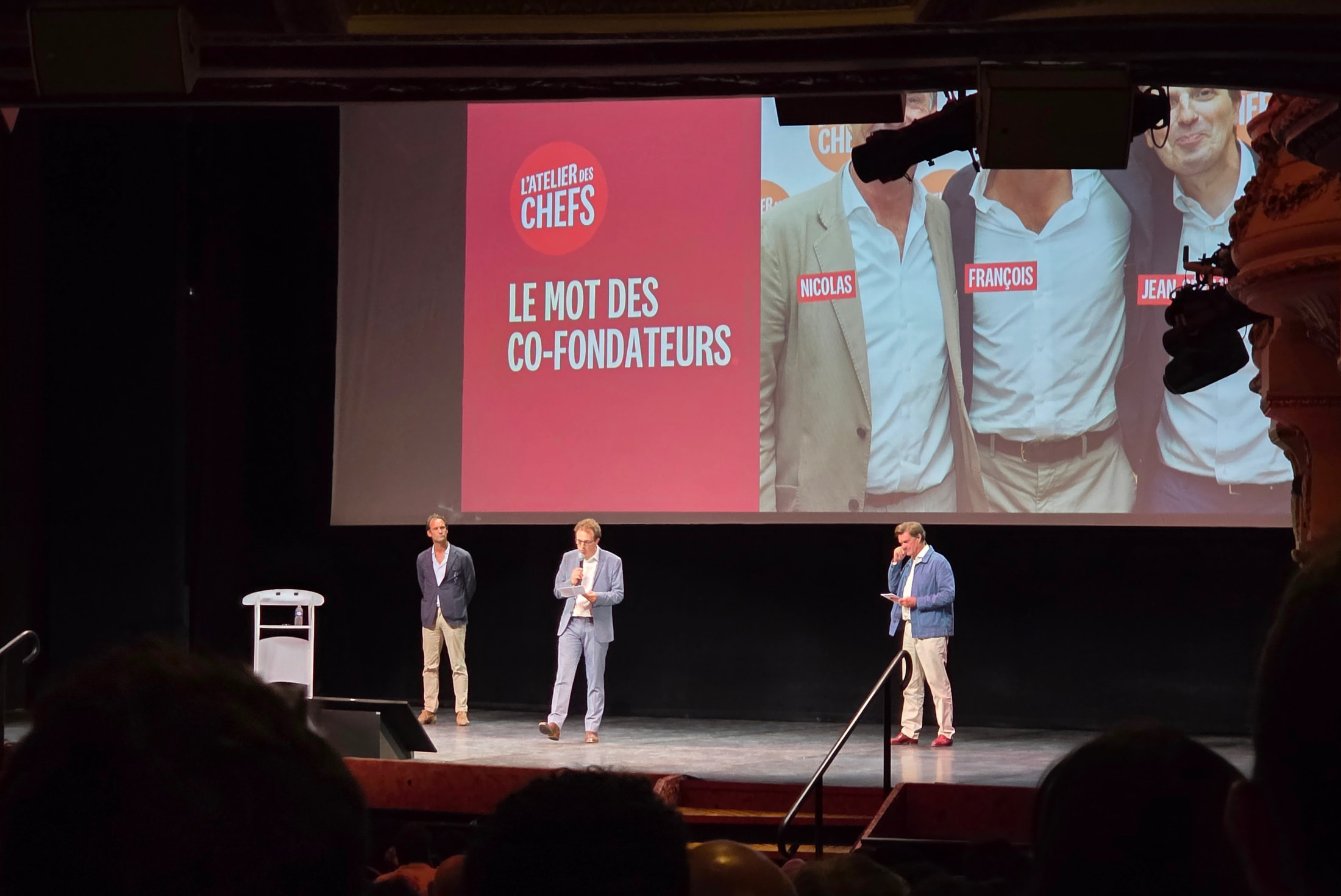 Sur la scène du Théâtre Mogador, les trois cofondateurs de L’Atelier des Chefs devant l’écran de projection de la promo 2026