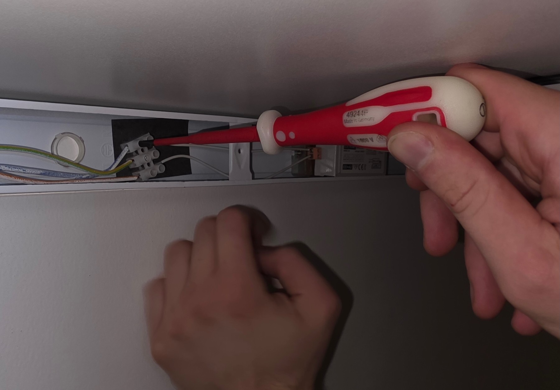 Tournevis isolé VDE 1 000 V serrant un connecteur au fond d’un profilé de luminaire au plafond