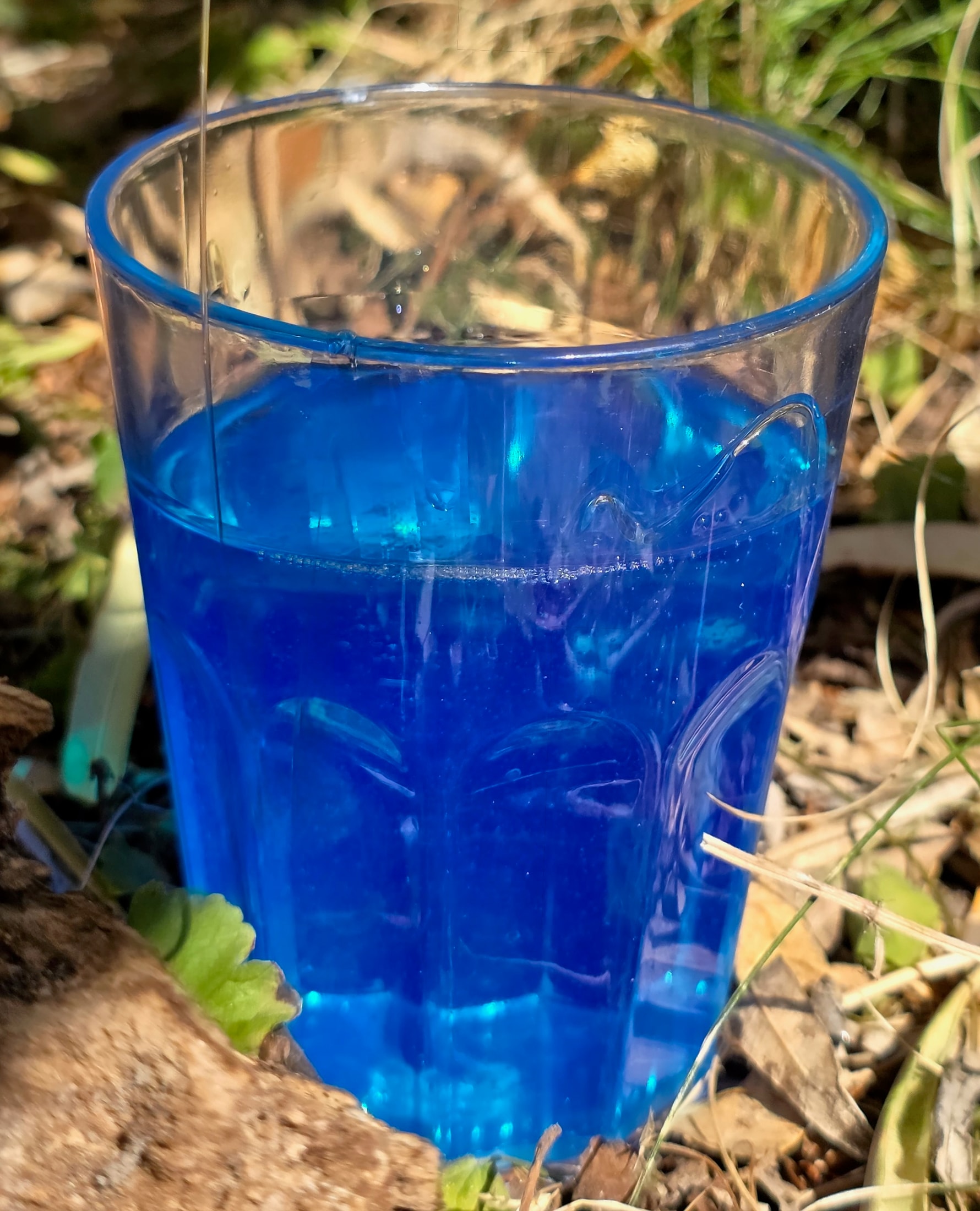 Verre transparent rempli de Magic Gel isolant bleu translucide posé sur le sol