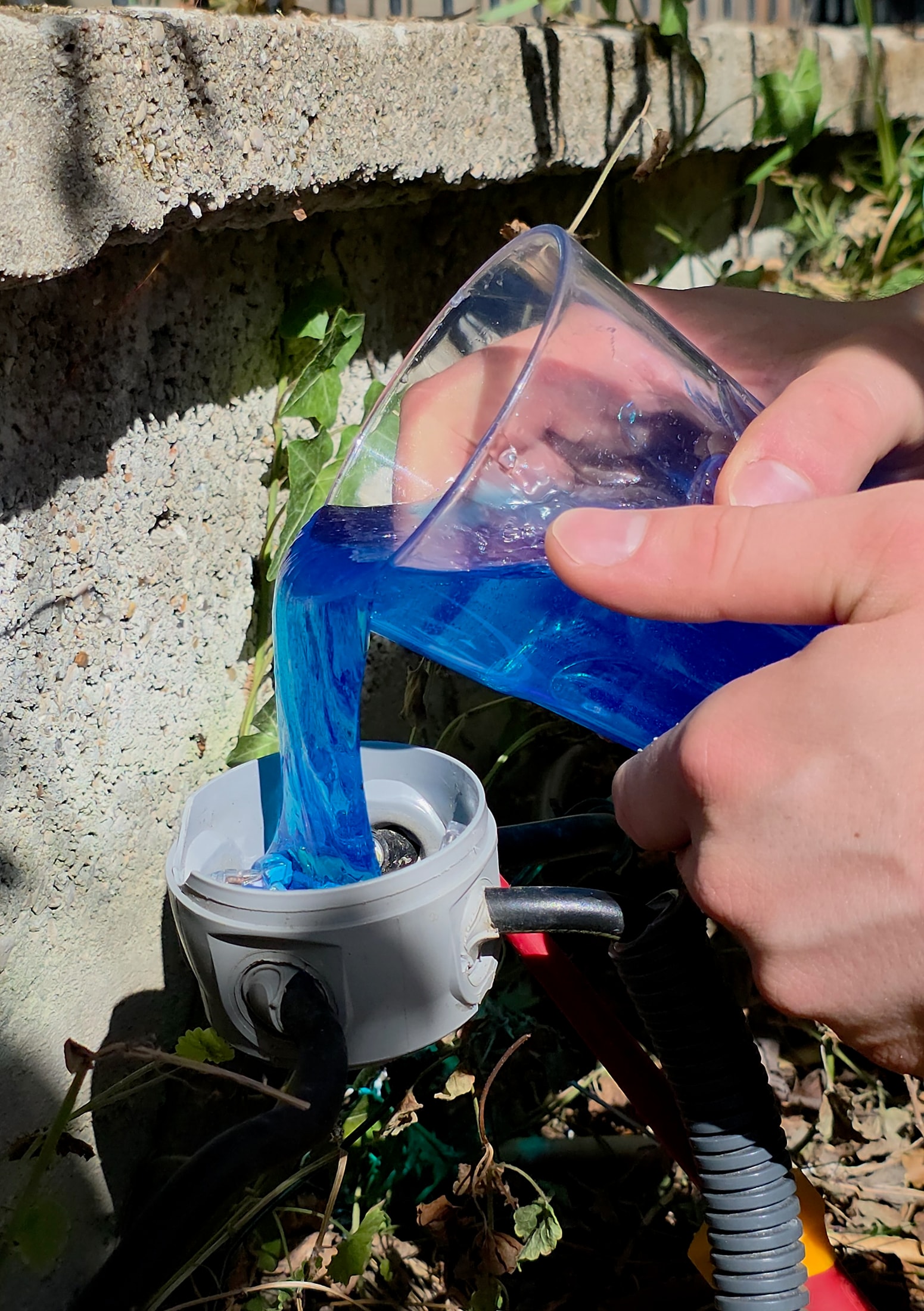 Versement du Magic Gel isolant bleu depuis un verre dans une boîte de dérivation ronde grise