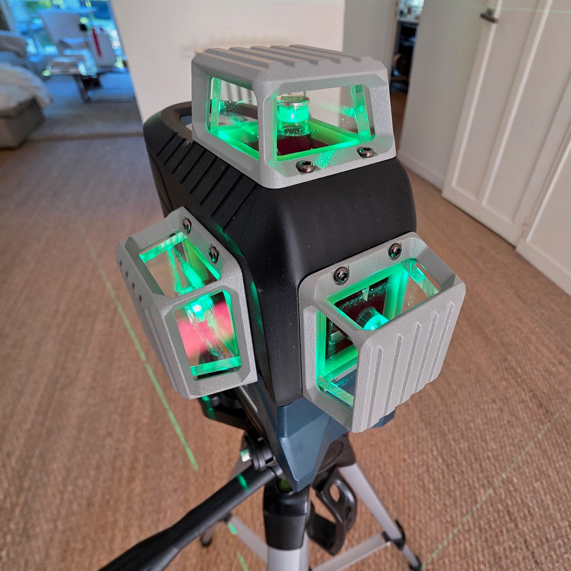 Niveau laser vert 360 degres allumé sur trépied dans un salon, lignes projetées sur les murs