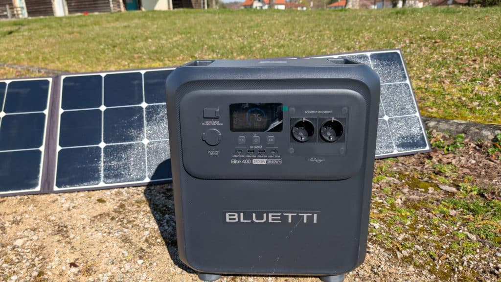 Station d’alimentation portable grise Bluetti Elite 400 posée sur le sol avec un panneau solaire pliable en arrière-plan.