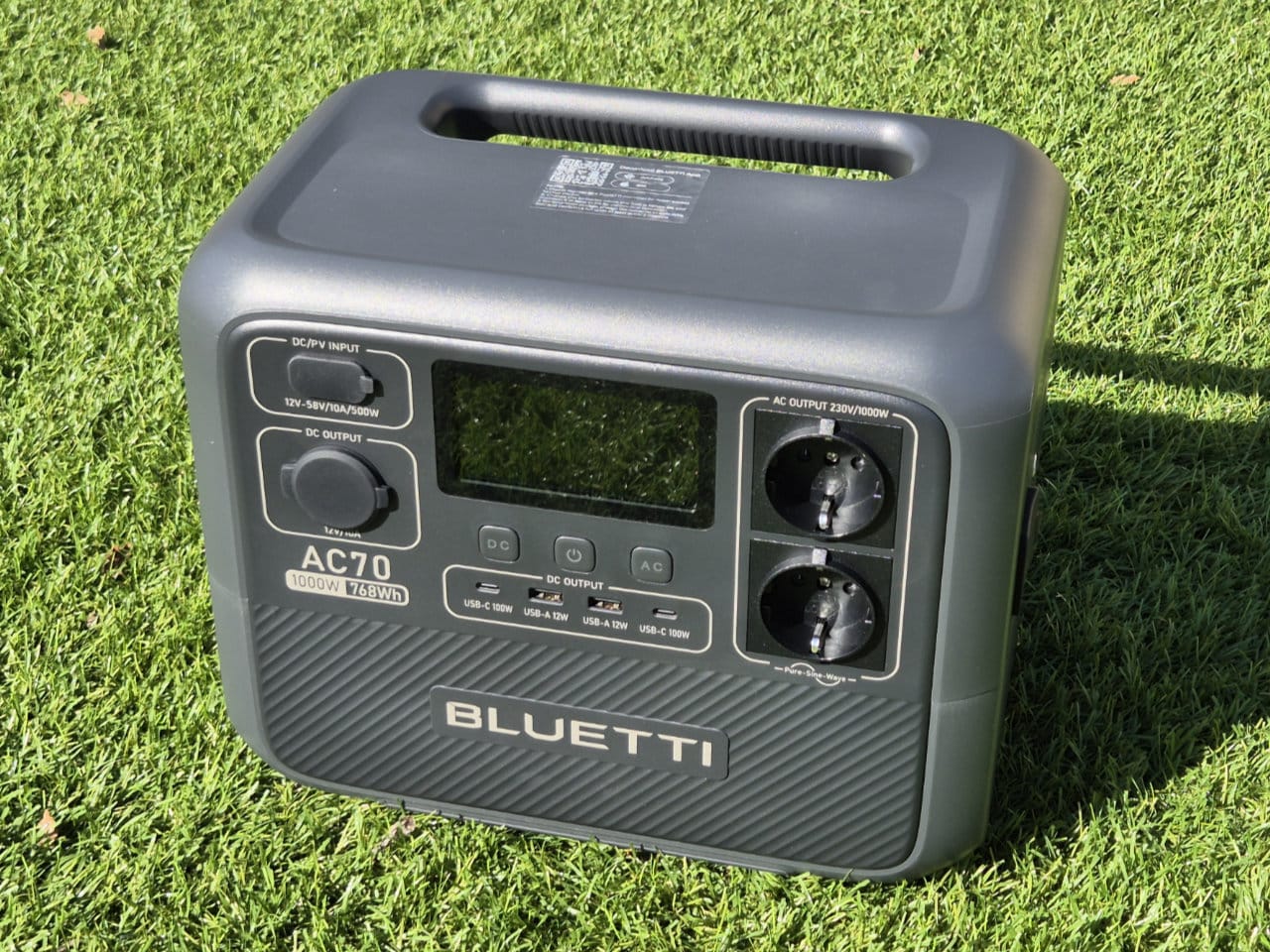 Station d’alimentation portable grise Bluetti AC70 posée sur une pelouse verte.