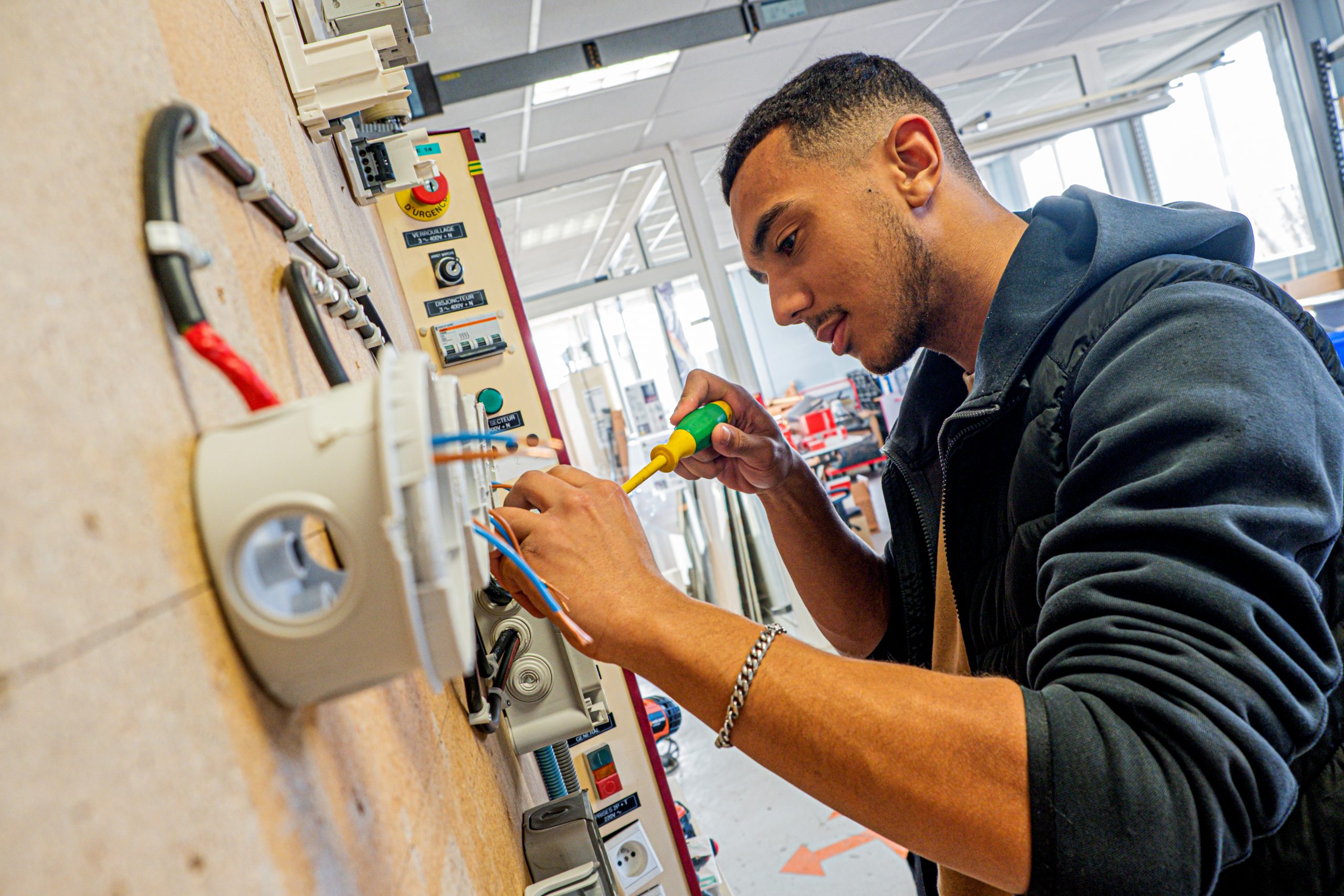 Un jeune homme utilisant un tournevis vert et jaune pour travailler sur un tableau électrique dans un atelier de formation
