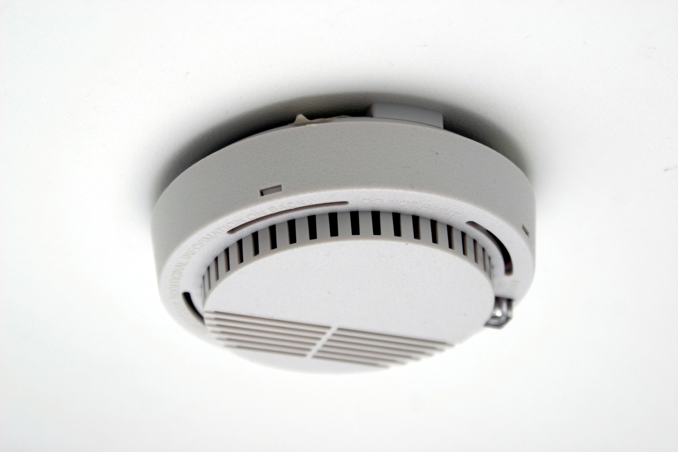 Un détecteur de fumée blanc rond fixé à un plafond blanc.