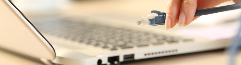Une main tenant un connecteur de câble ethernet au-dessus du port réseau d’un ordinateur portable.