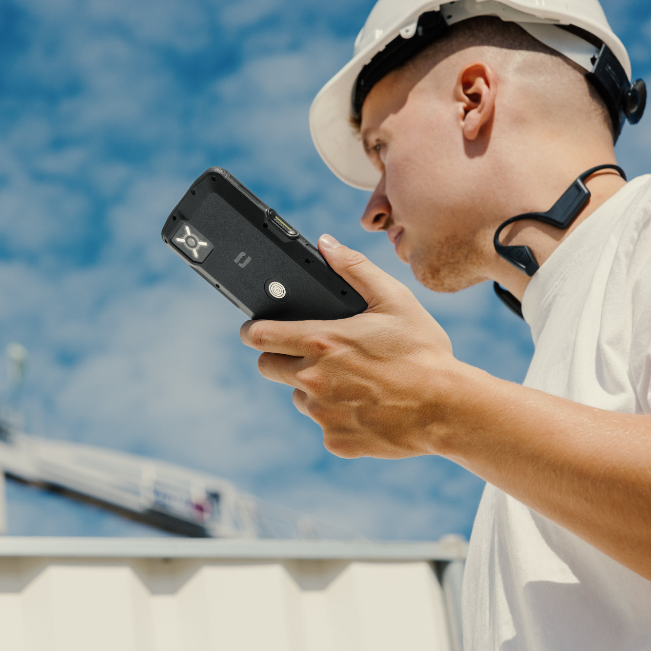 Homme portant un casque de chantier blanc tenant un smartphone noir robuste Crosscall Core-M6 sur un chantier.