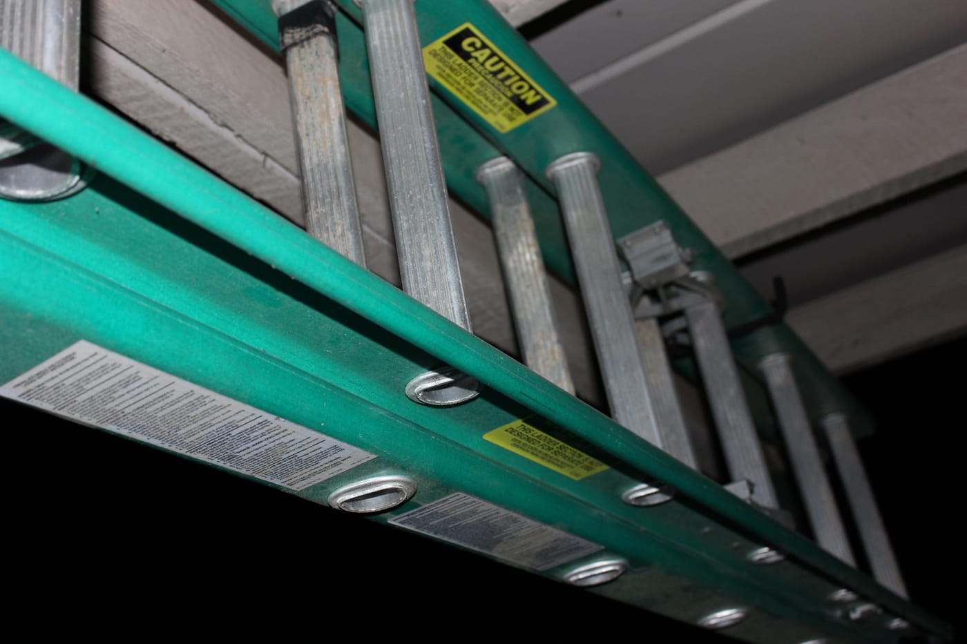 Gros plan d’une échelle en fibre de verre verte vue de dessous, avec échelons en aluminium et étiquettes de sécurité jaunes