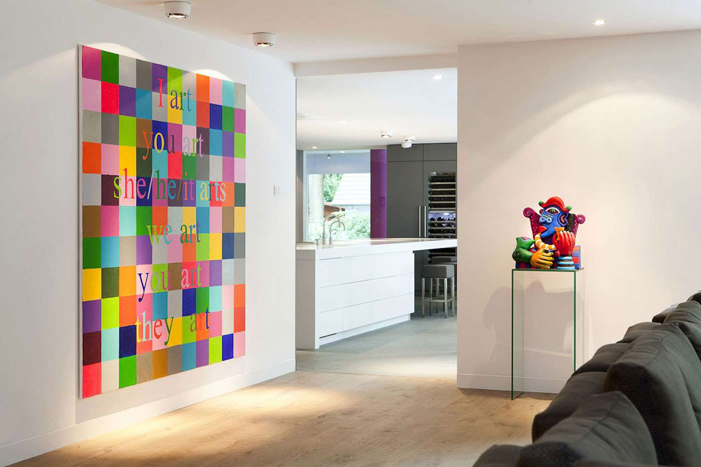 Un intérieur lumineux avec un grand tableau coloré accroché au mur et éclairé par des spots encastrés au plafond, à proximité d’un canapé et d’une sculpture.
