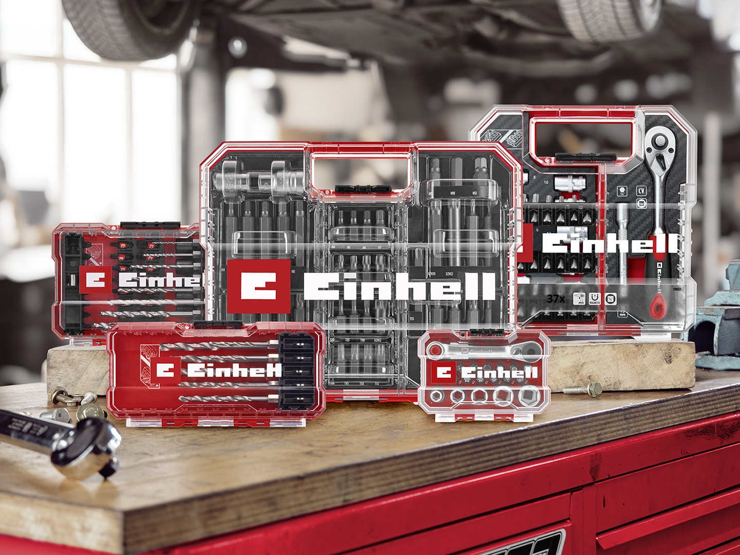 Plusieurs coffrets d’accessoires d’outillage Einhell disposés sur un établi rouge dans un garage.