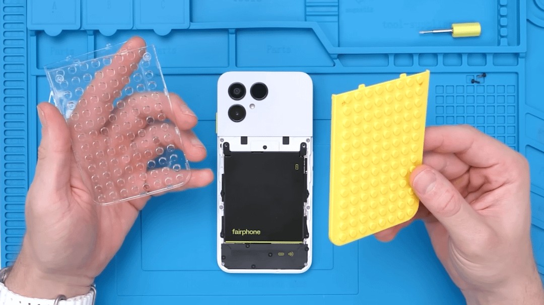 Fairphone blanc démonté avec deux coques personnalisées tenues dans les mains sur un tapis de travail bleu