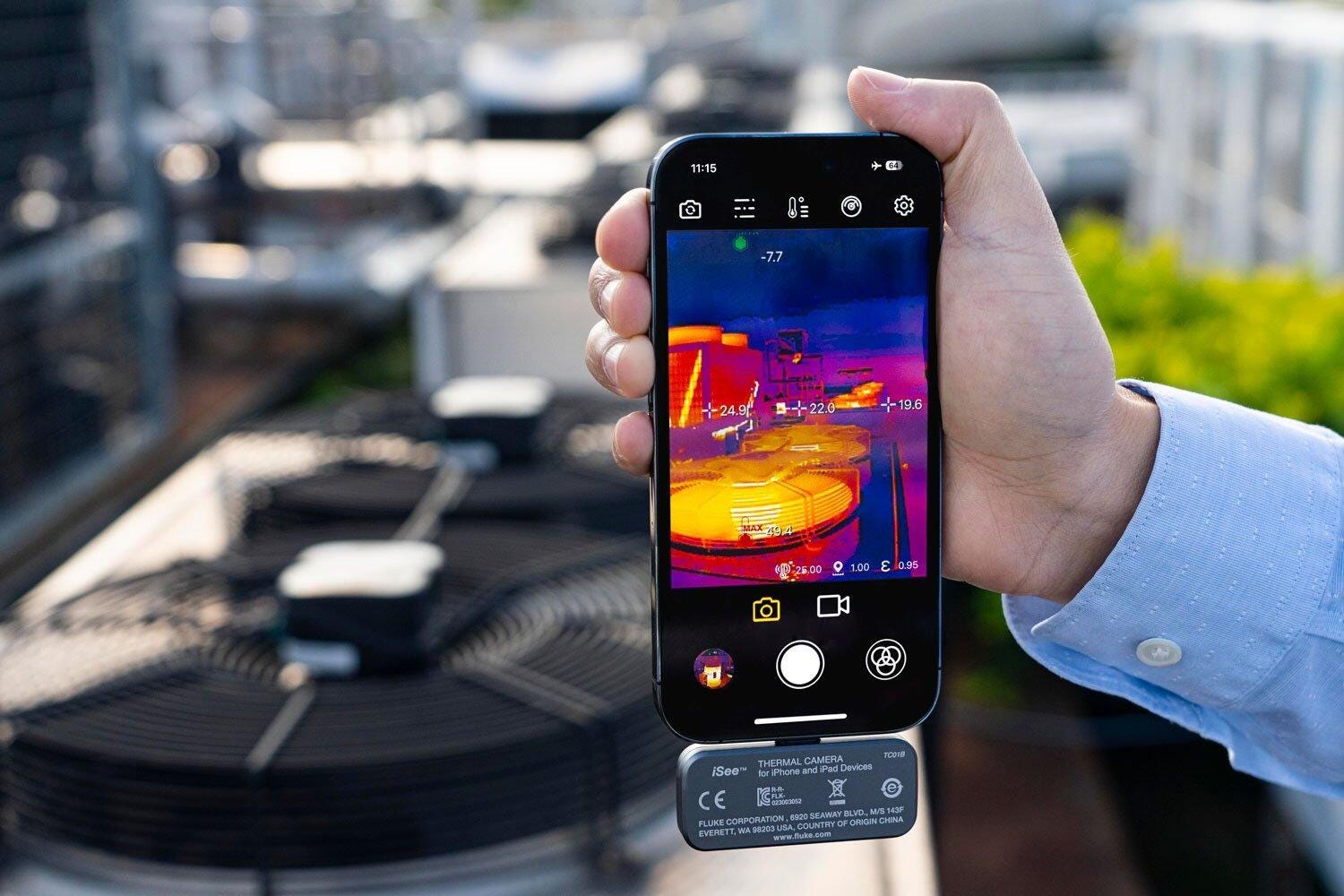 Une main tenant un smartphone affichant une image thermique avec un accessoire iSee THERMAL CAMERA connecté en bas.