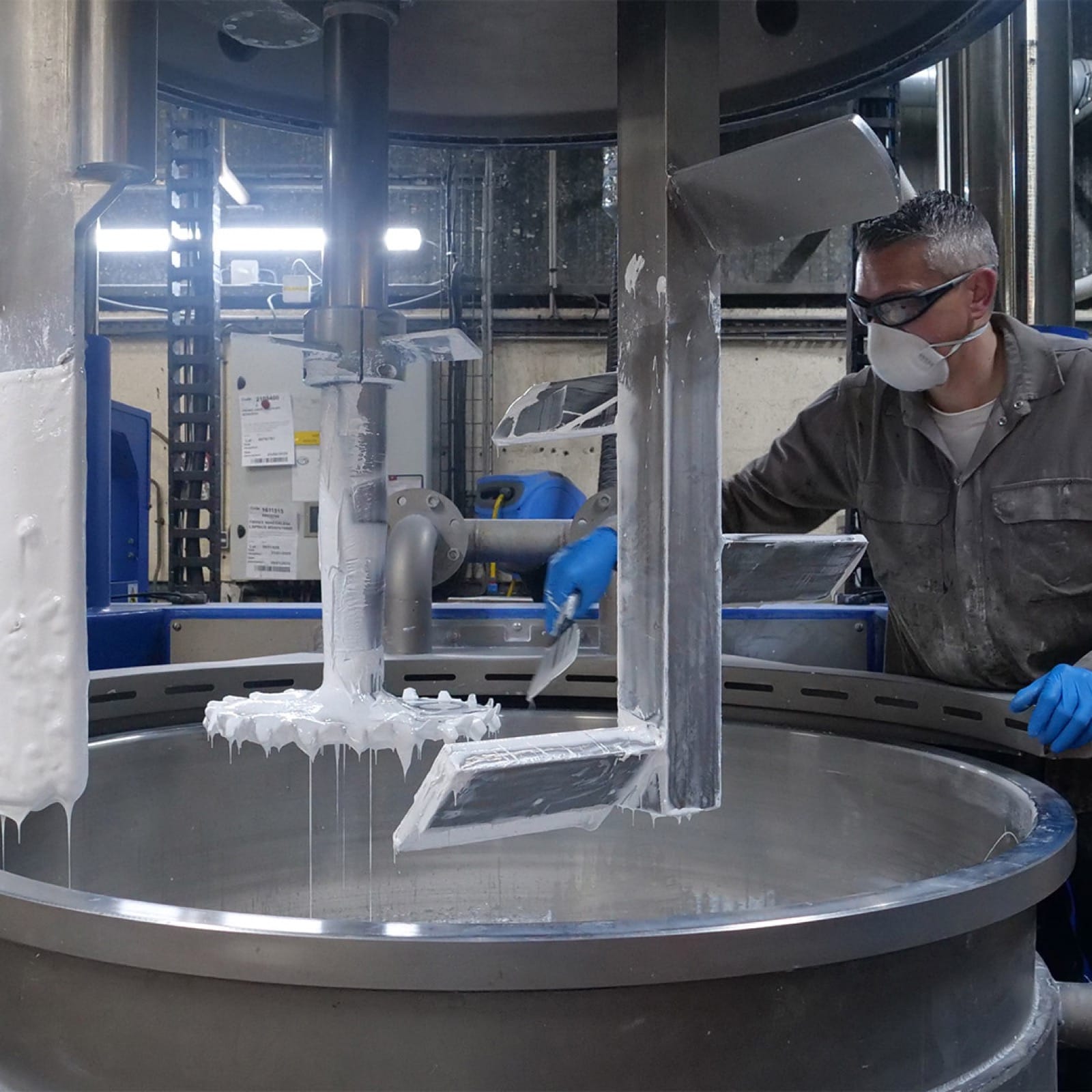 Opérateur GEB en masque et gants nettoyant l'agitateur d'une cuve de fabrication de mastic blanc