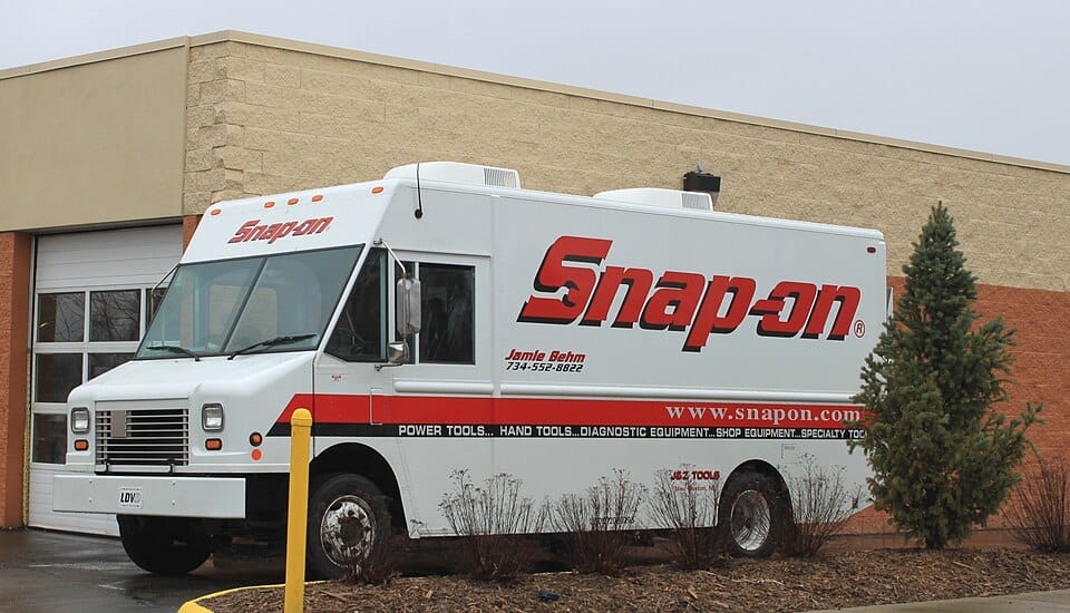 Fourgonnette blanche de concessionnaire Snap-on stationnée devant un garage