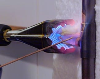 Chalumeau équipé d'un embout Cercoflam en cours de brasage d'un tube de cuivre, avec la flamme enveloppant le raccord