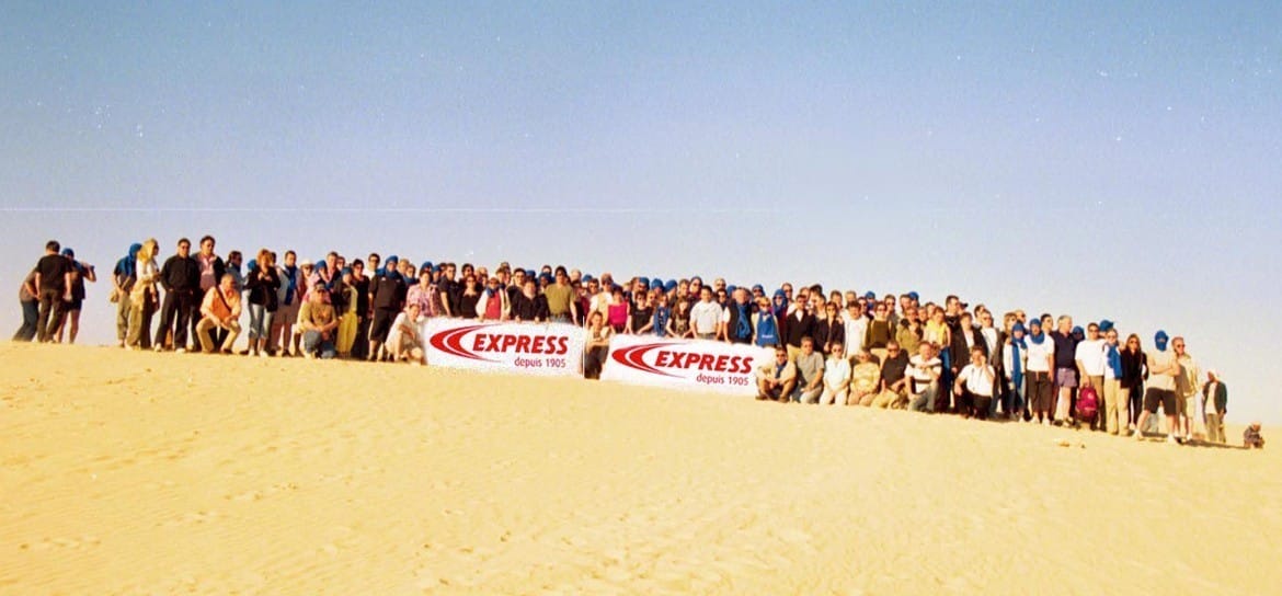 Groupe de collaborateurs Guilbert Express posant avec une banderole de la marque dans le désert du Sahara