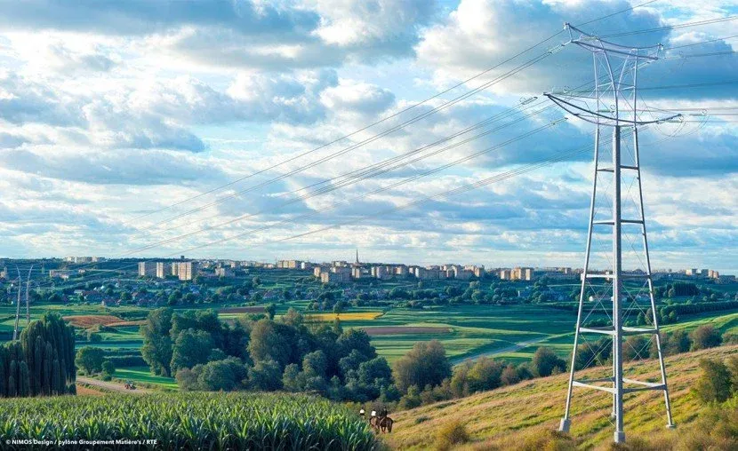 Pylône de ligne haute tension au-dessus de champs près d’une ville