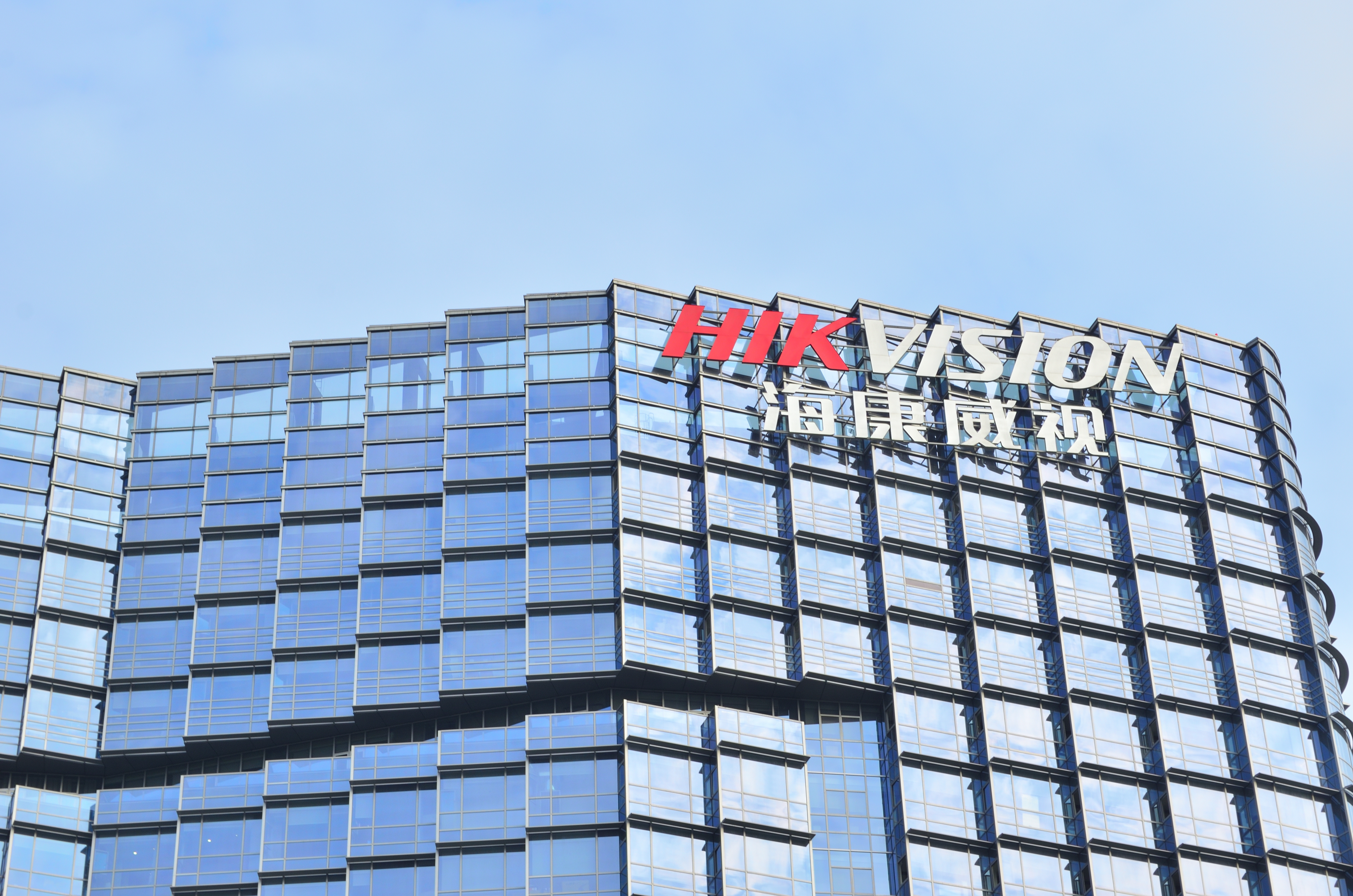 La façade vitrée d'un bâtiment moderne surmontée du logo HIKVISION et de caractères chinois.